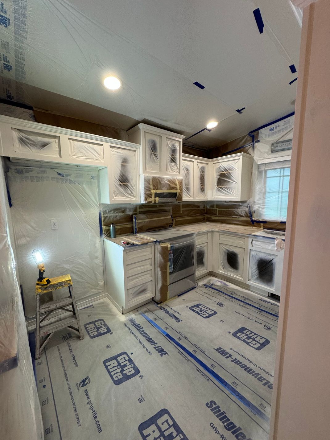 Renovated white kitchen with cabinets, countertops, and appliances under construction, floor protected by plastic coverings