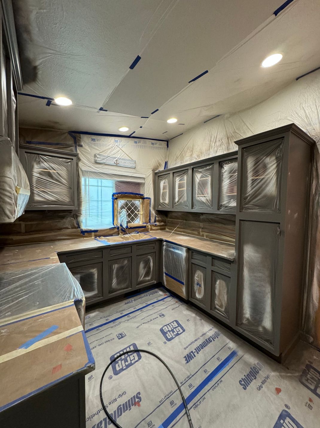 Modern kitchen under renovation with dark cabinets, exposed ceiling, and protective floor covering