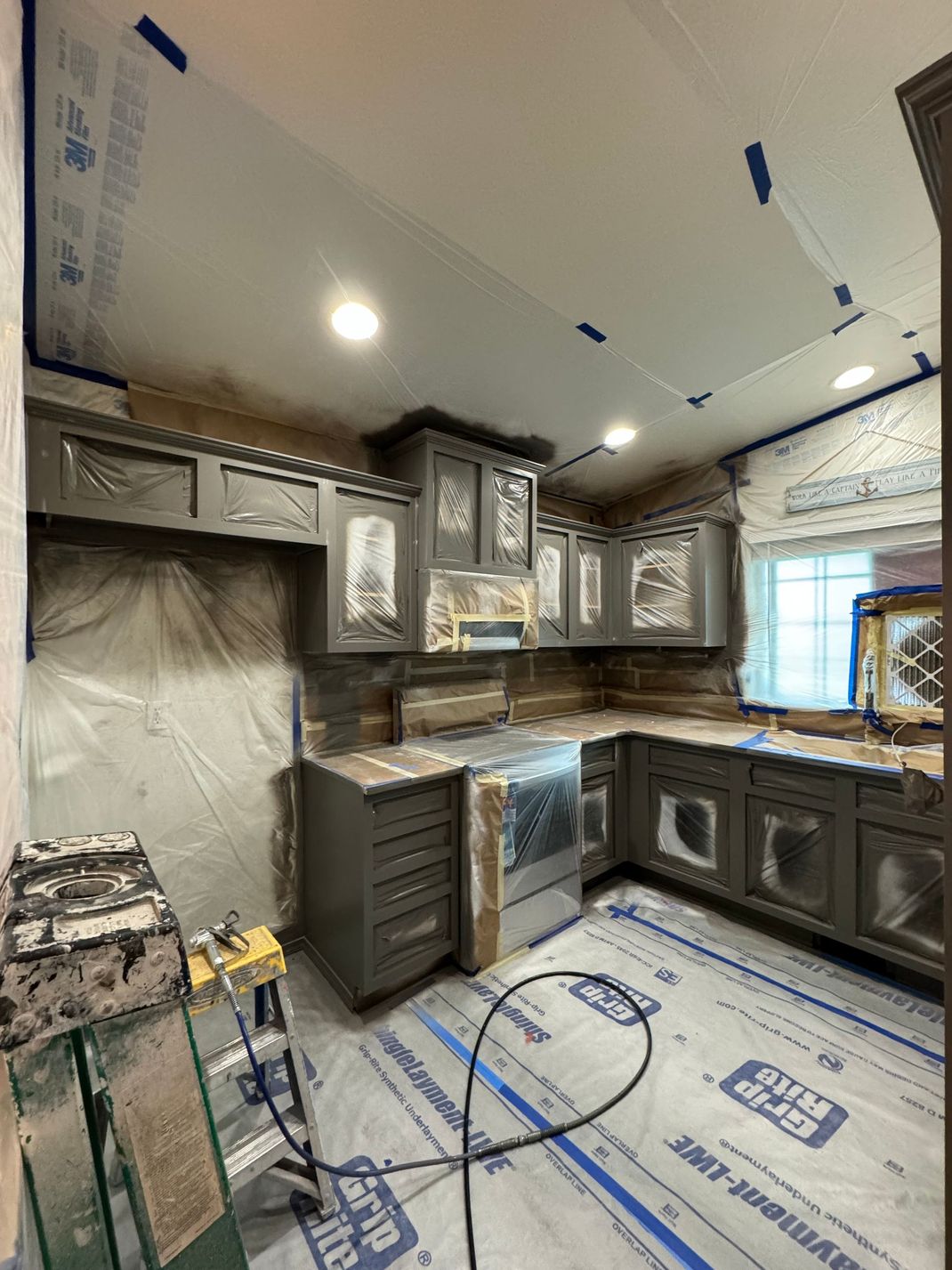 Kitchen under construction with gray cabinets, tiled backsplash, covered appliances, and protective floor covering
