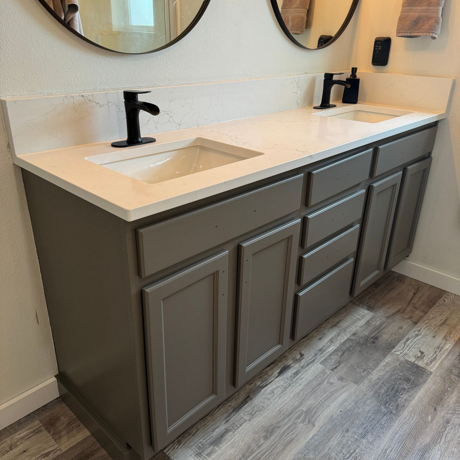 Modern bathroom vanity with double sinks, dark gray cabinets, and white countertop under round mirrors