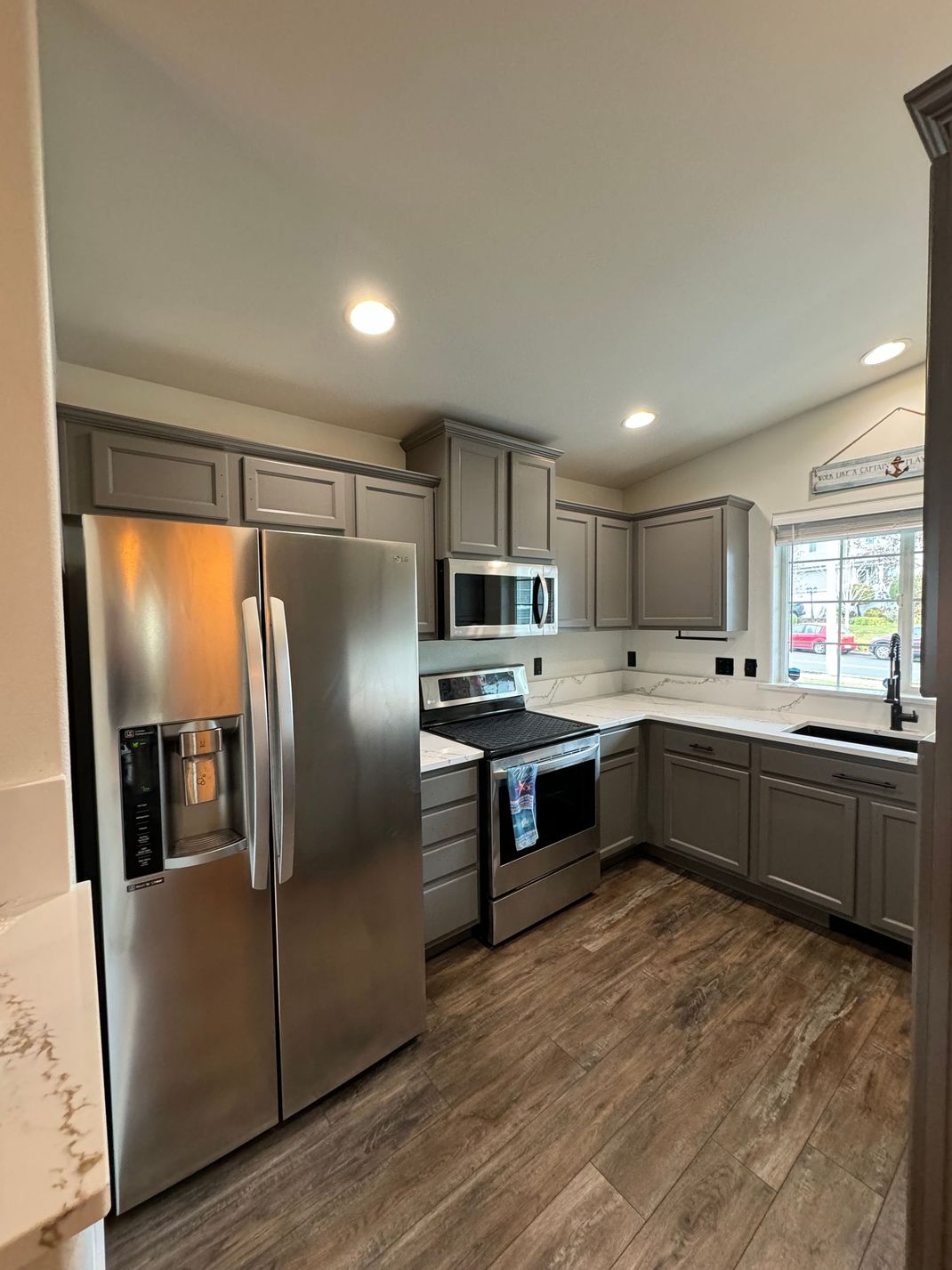 Modern kitchen with stainless steel appliances, gray cabinets, white countertops, and wood-look flooring.