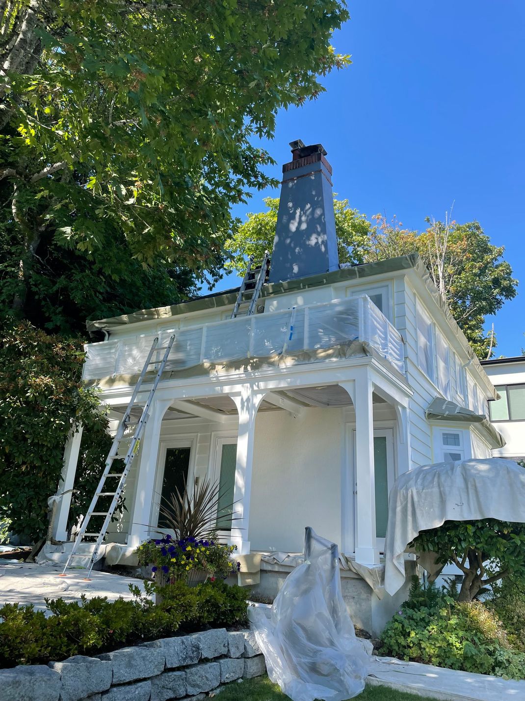 White house with porch and chimney, surrounded by lush green trees under a clear blue sky