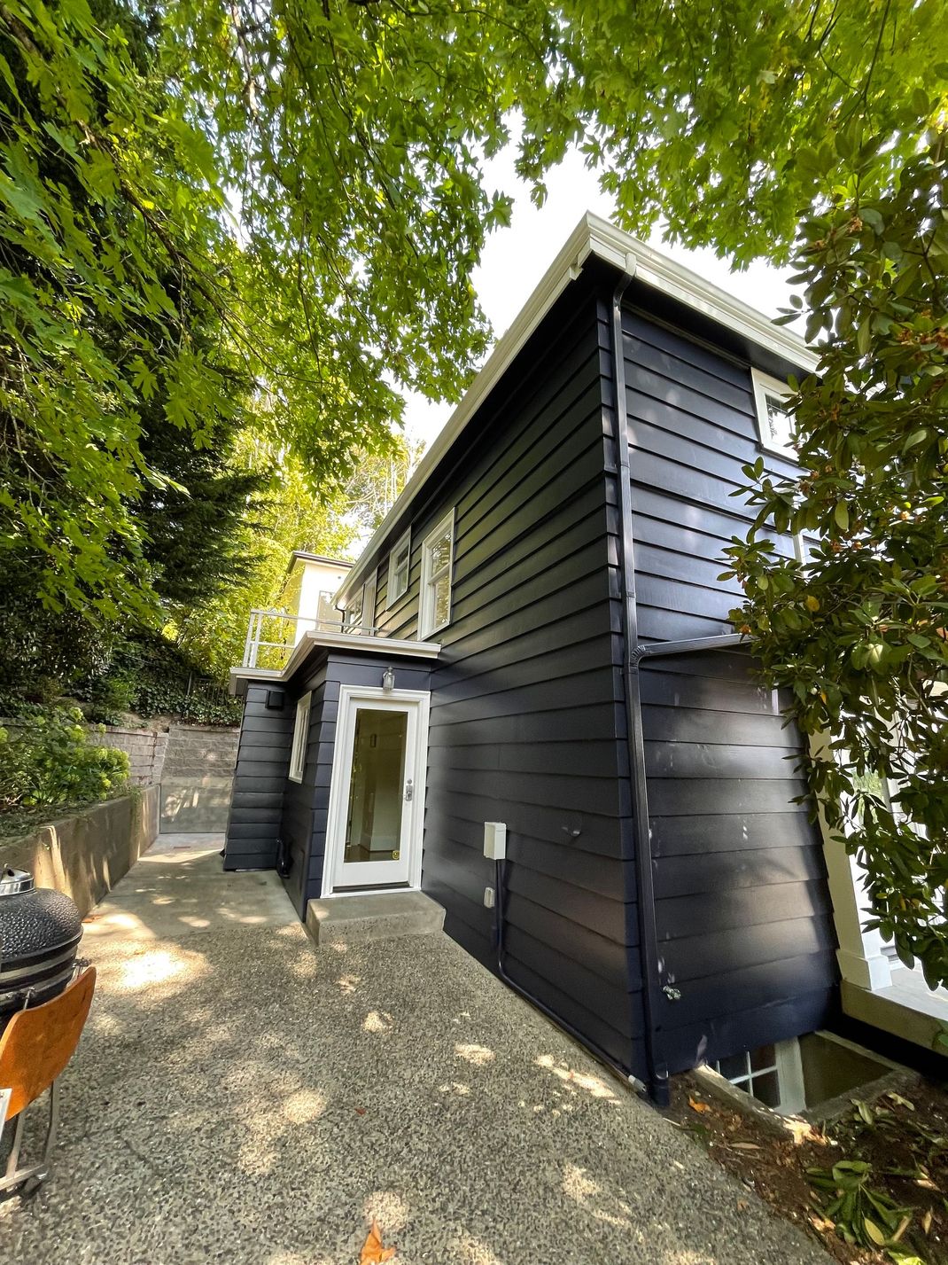 Black wooden house with white trim beside a gravel path under leafy trees