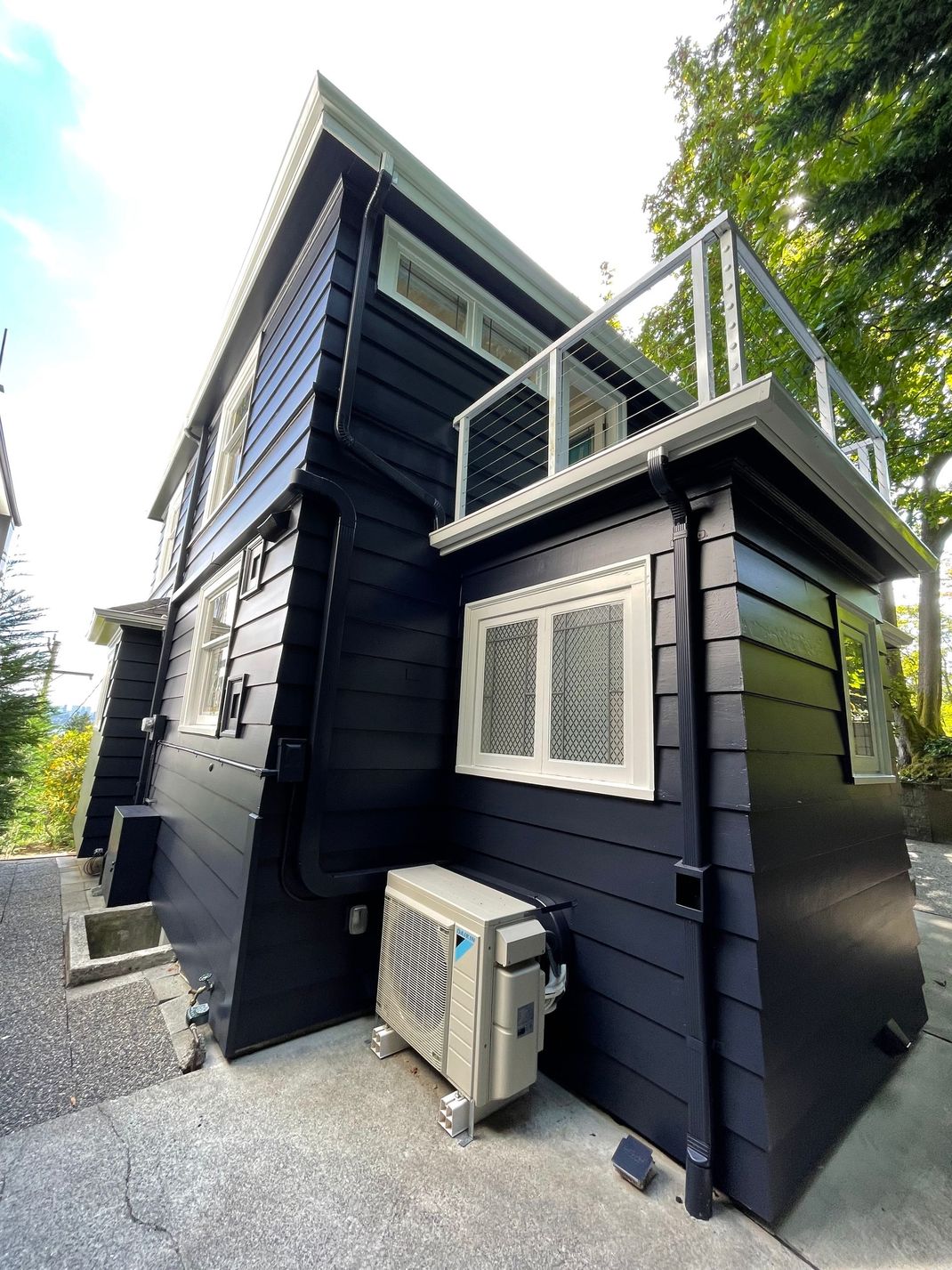 Black house exterior with white-trimmed windows, side balcony, and an air conditioner unit on gravel.