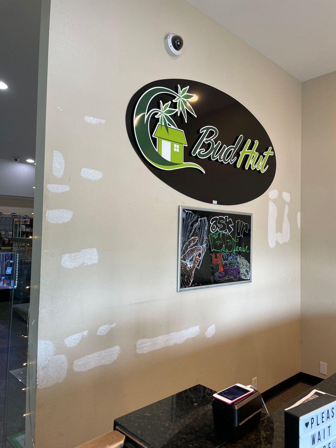 Wall with a round “BudTru” sign above a smaller floral sign in a bright indoor lobby.