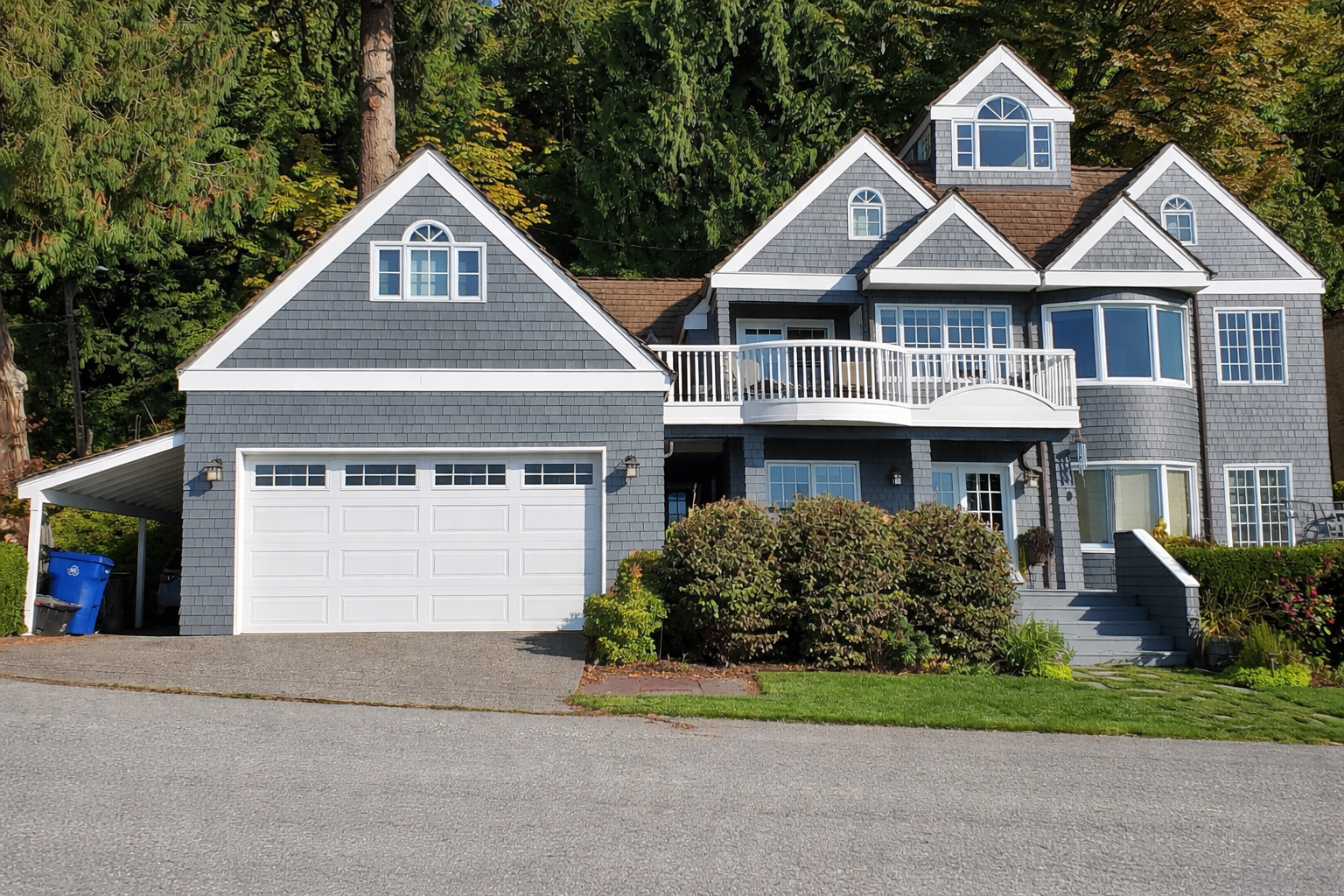 Gray suburban house with white trim, attached garage, and front porch behind shrubs and trees