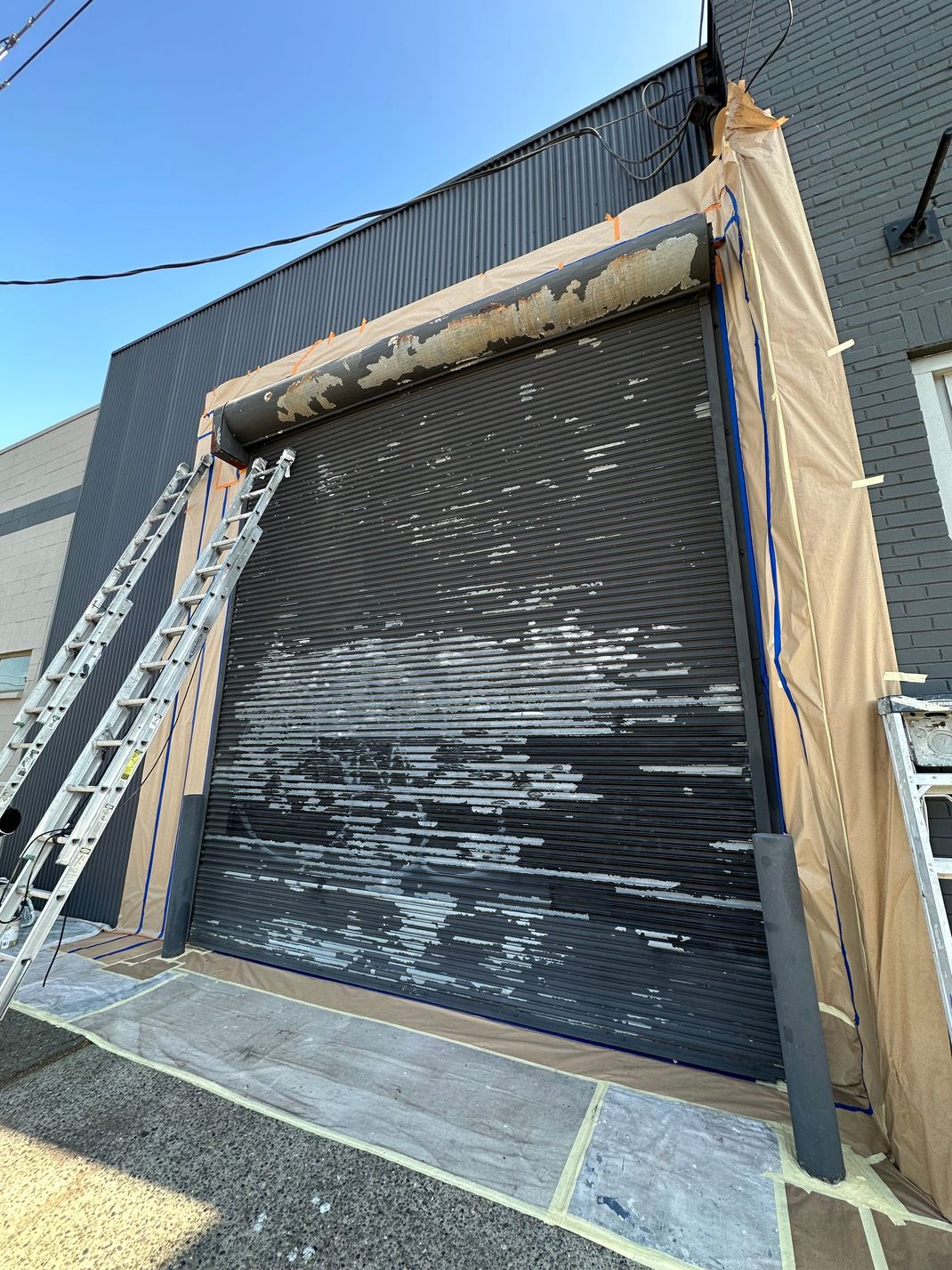 Building exterior with a partially raised black roll-up door, ladders, and renovation materials.