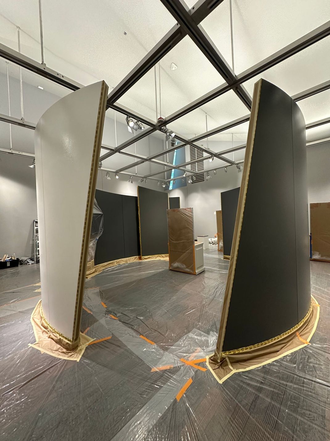 Indoor art installation with tall curved panels, ropes, and a central hanging object in a gallery space