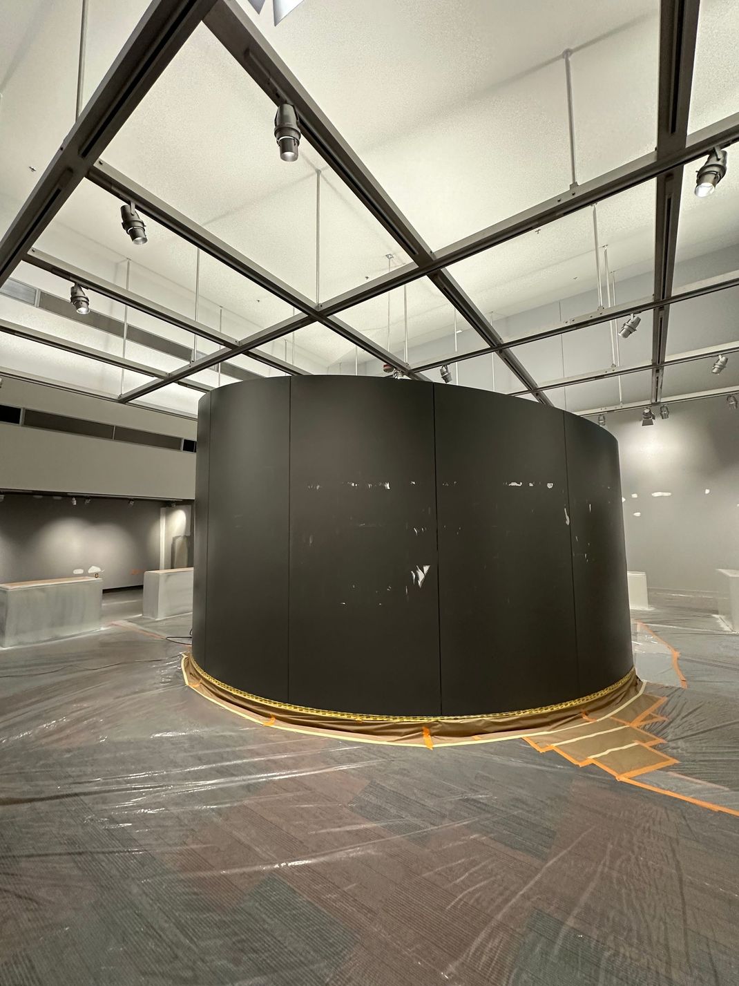 Large black cylindrical structure in a spacious industrial gallery with track lighting and concrete floor