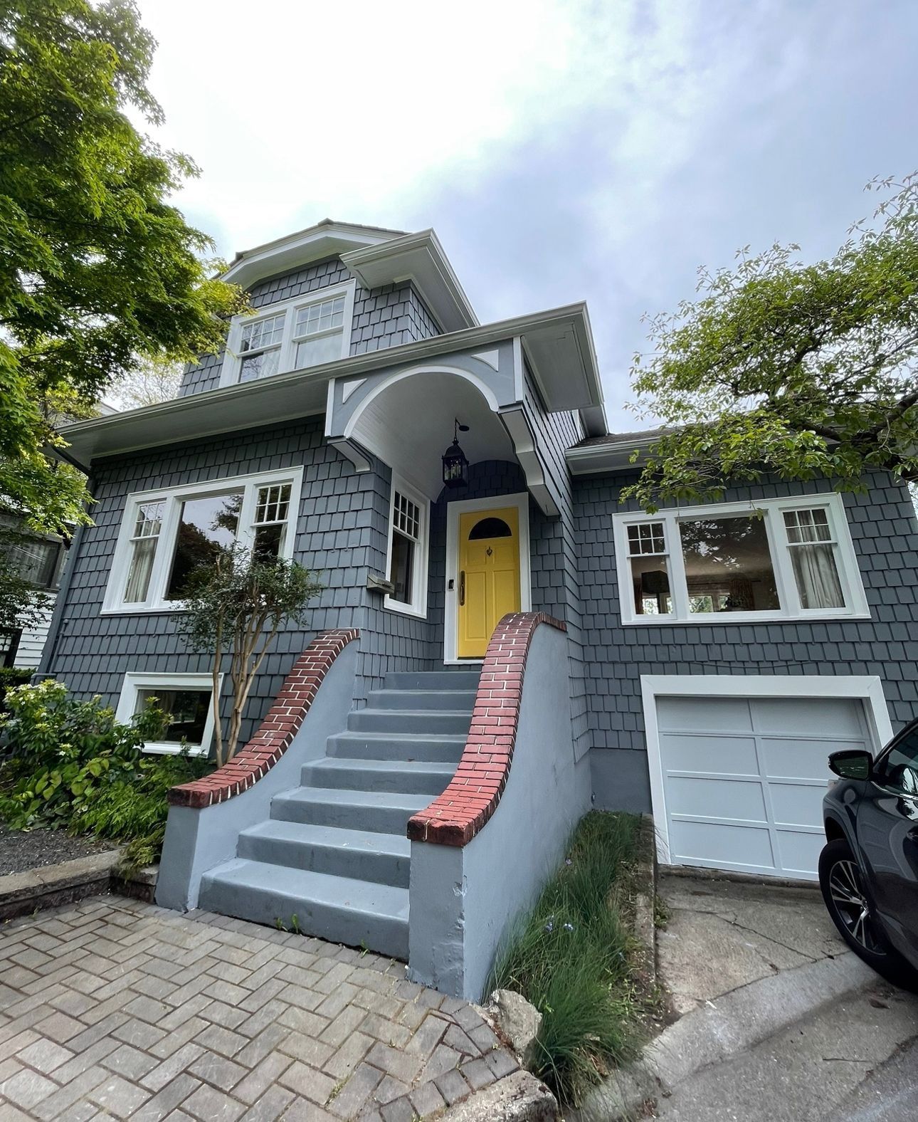 A gray shingled house with a bright yellow front door, a prominent front staircase, and an integrated garage.