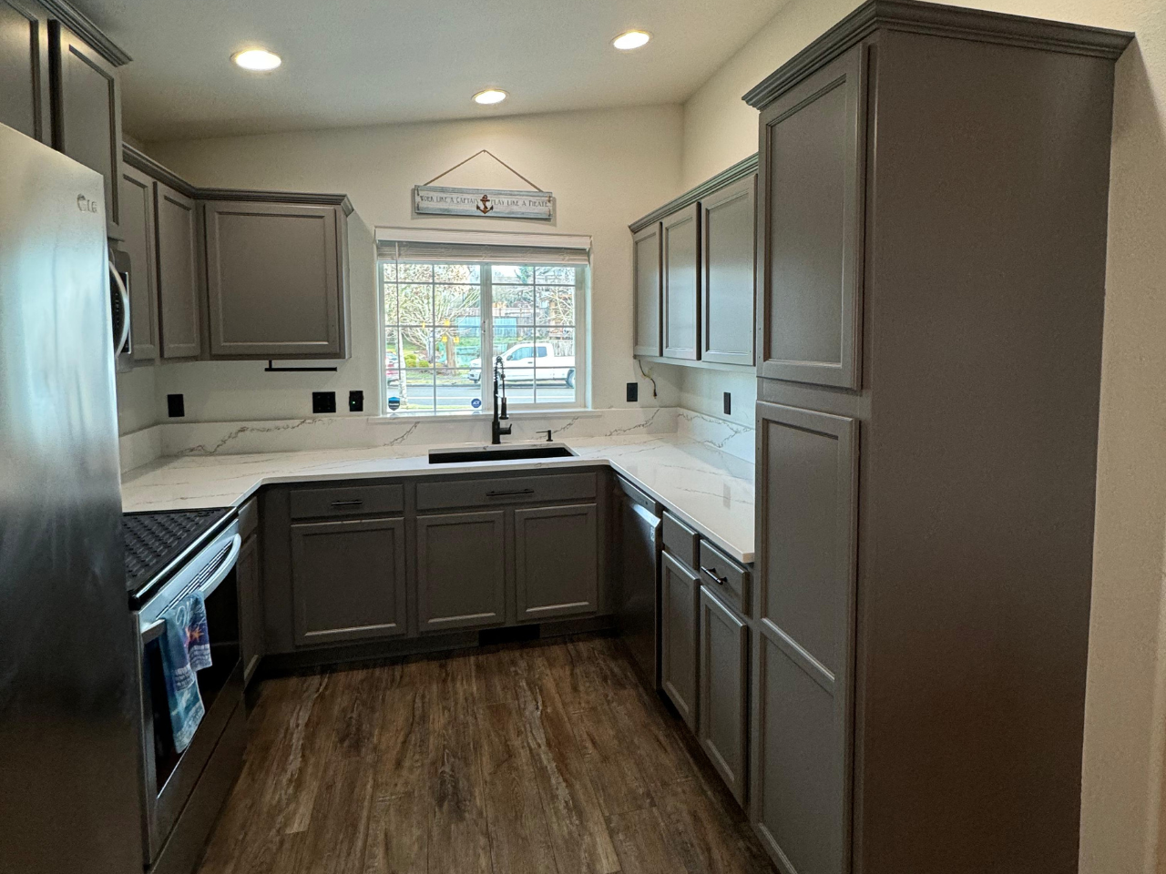 A modern kitchen featuring gray cabinets, light countertops, stainless steel appliances, and wood-look flooring.