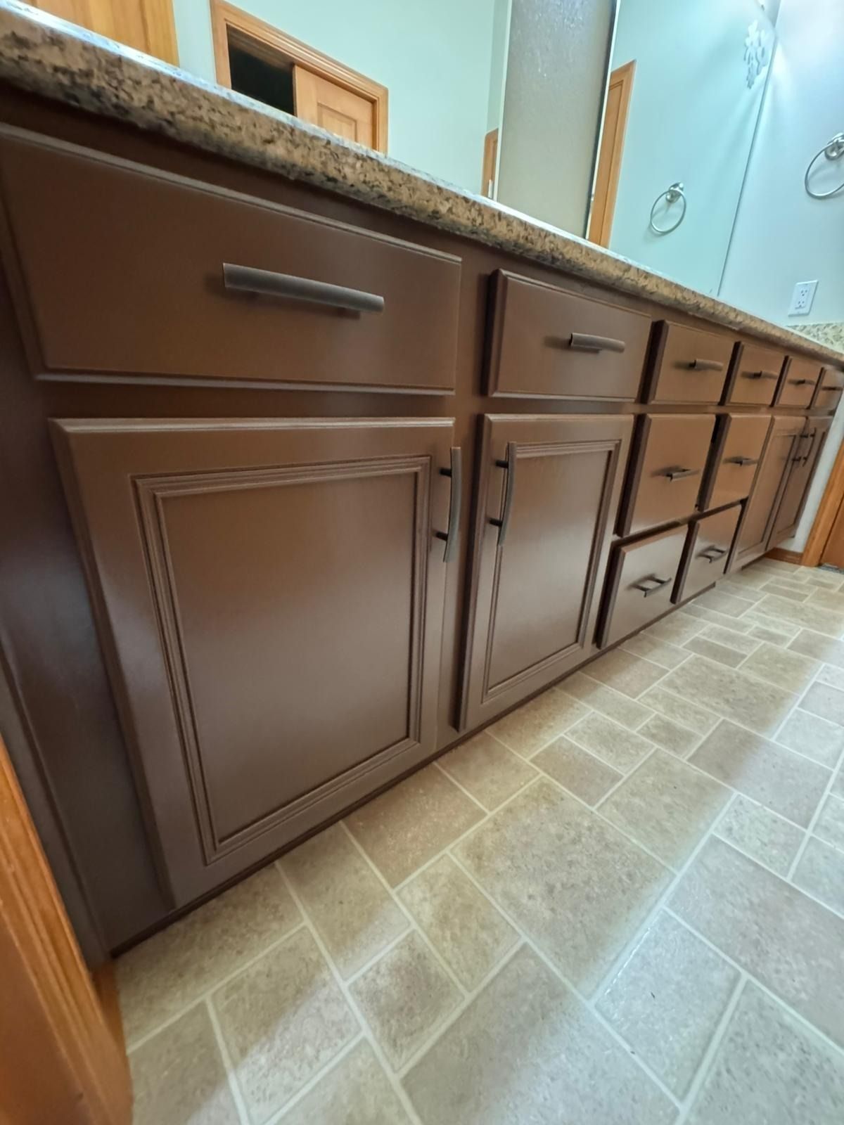 Brown bathroom vanity cabinets with a granite countertop and tiled floor.