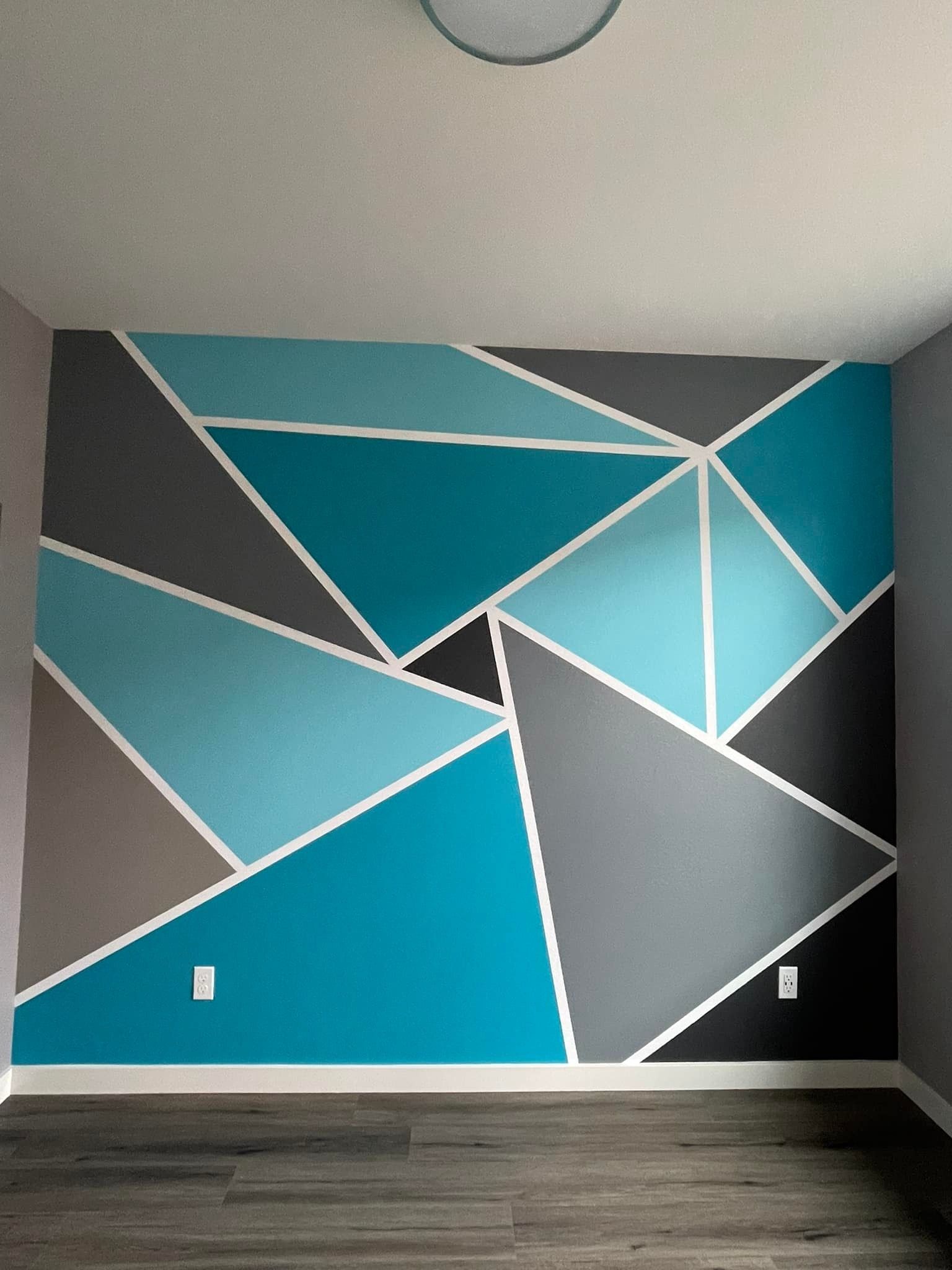 A room wall featuring a geometric mural of triangles in varying shades of blue, gray, and dark teal separated by white lines.