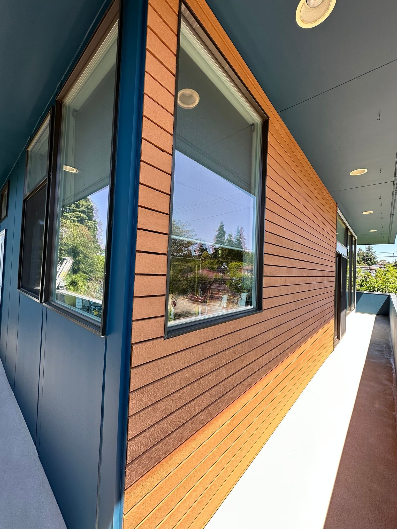 A wide-angle shot of a building exterior featuring wood-paneled walls, large windows, and a blue metal walkway overhang.