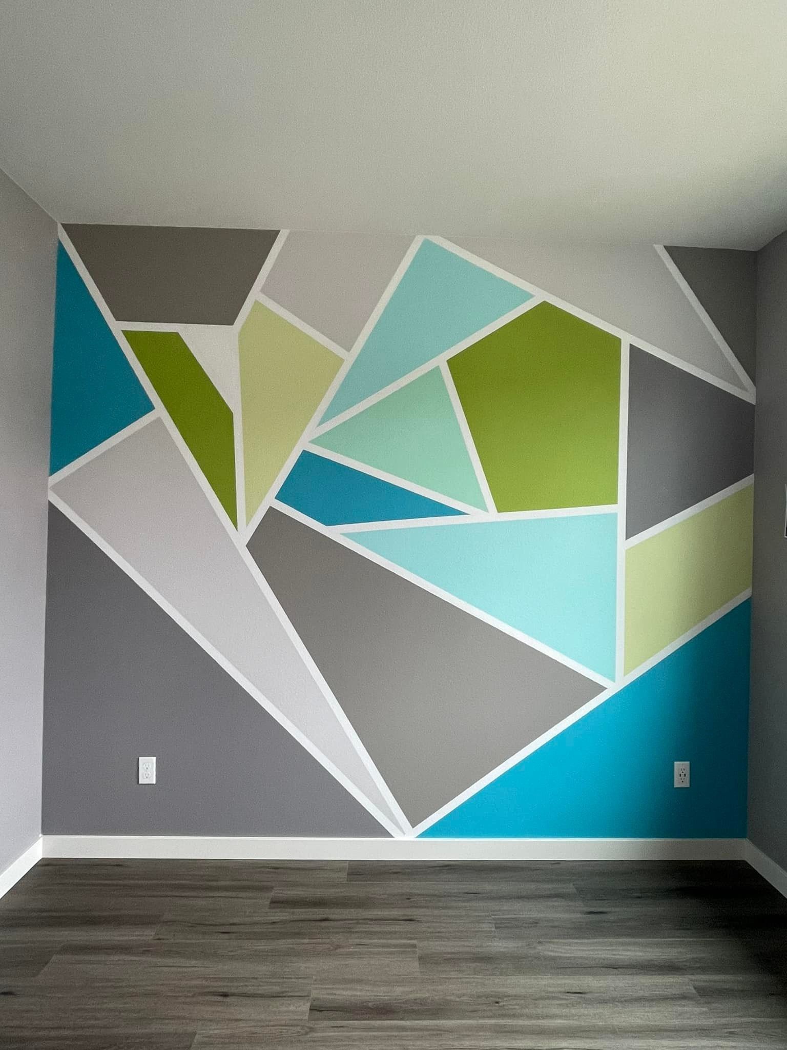 An accent wall features a geometric mural of triangles in shades of grey, bright blue, lime green, and pale mint.