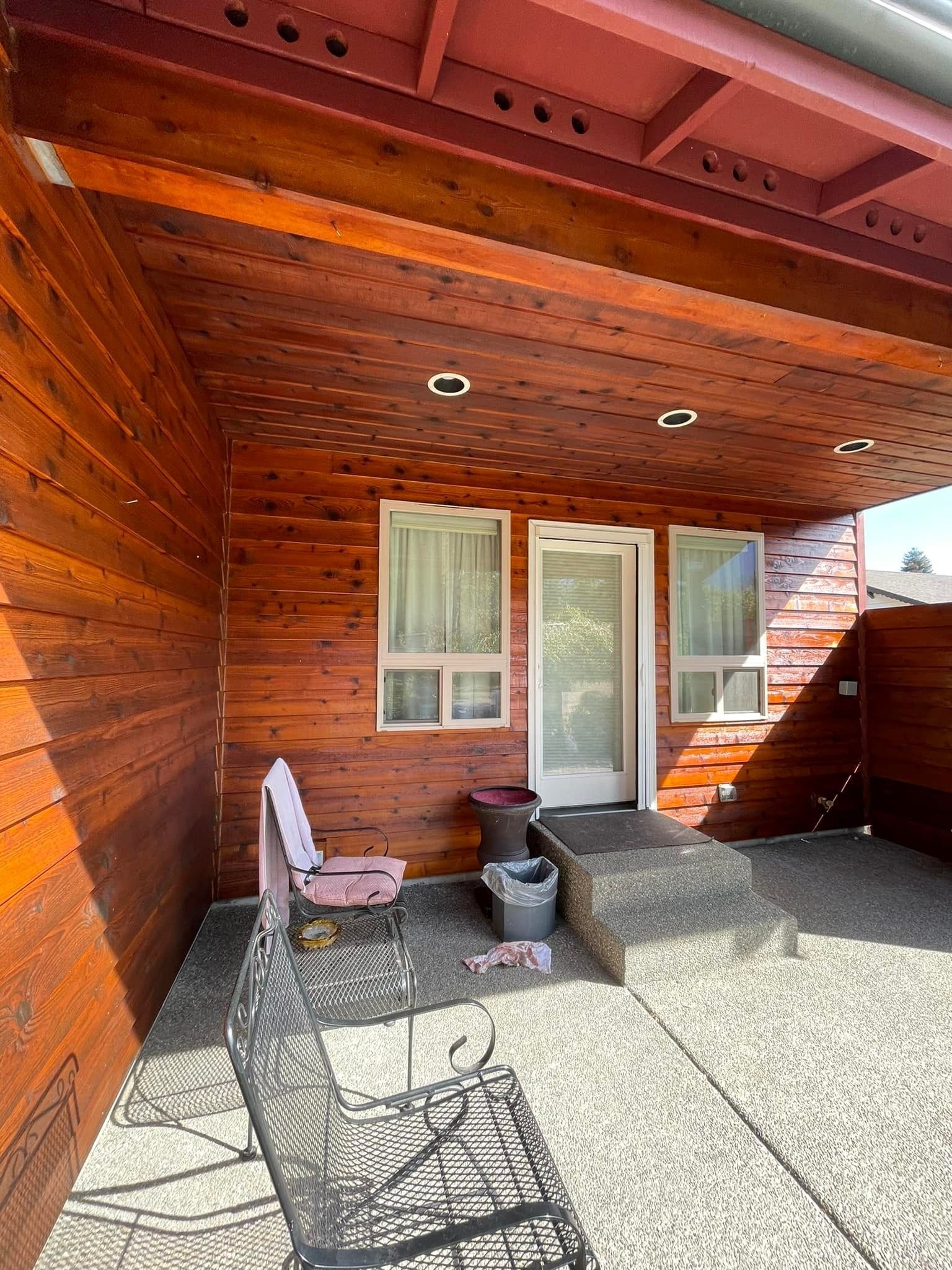 A covered patio with wood-paneled walls and ceiling, two metal chairs, and a sliding glass door.