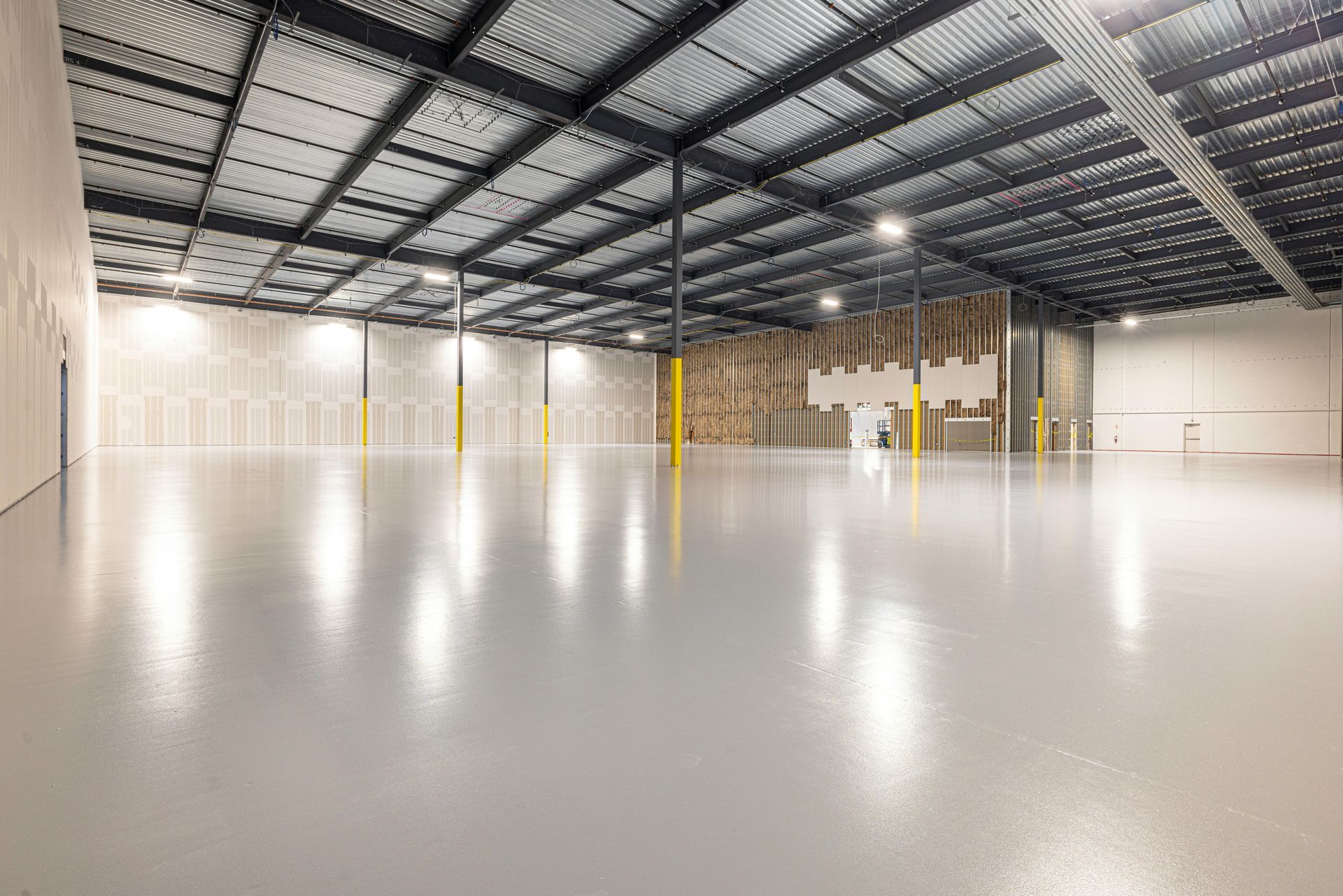 Empty industrial warehouse with polished concrete floor, exposed steel beams, and yellow support columns