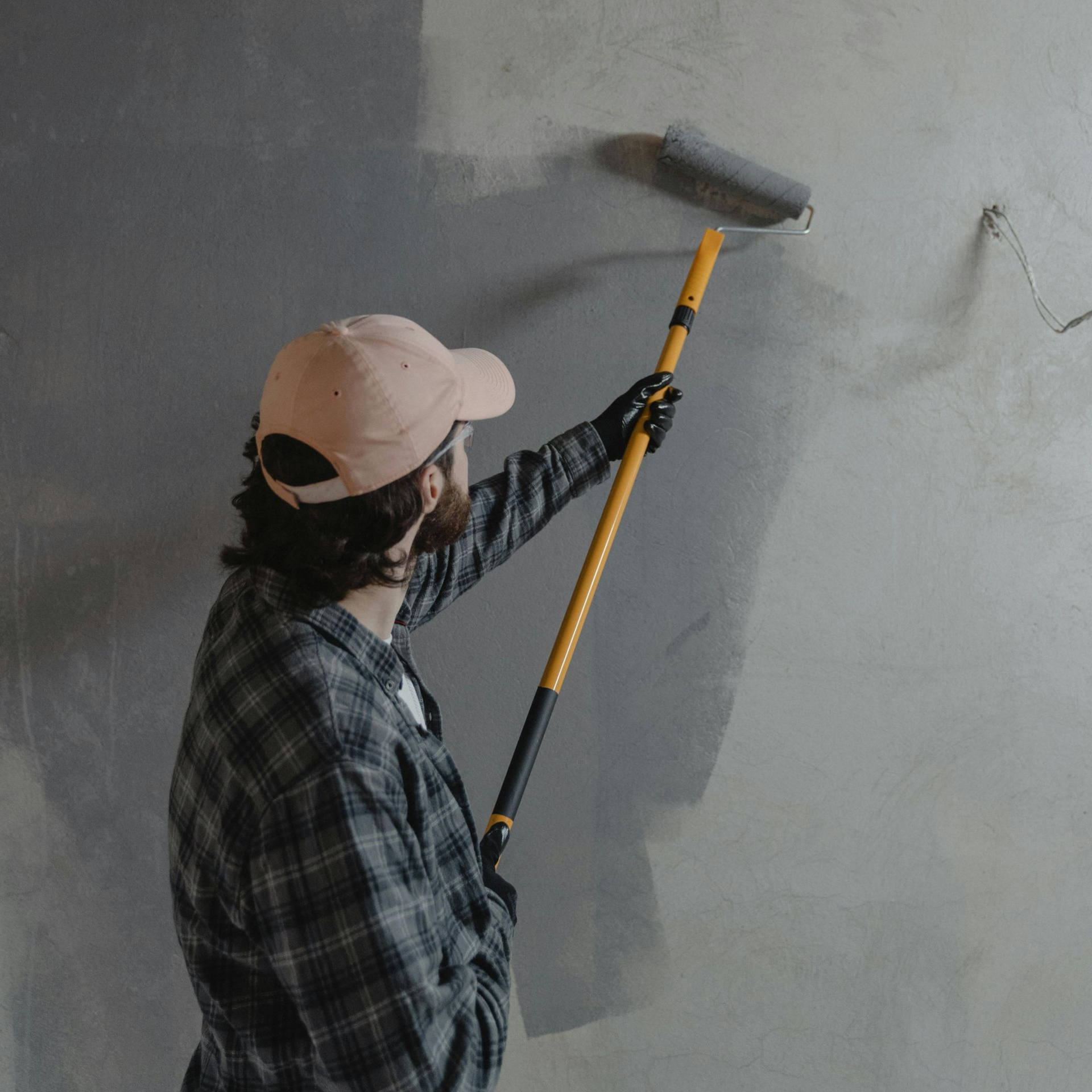 Person painting a gray wall with a roller on a long handle