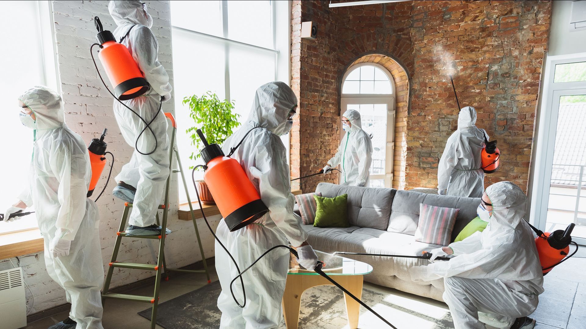 A group of people in protective suits are disinfecting a living room.
