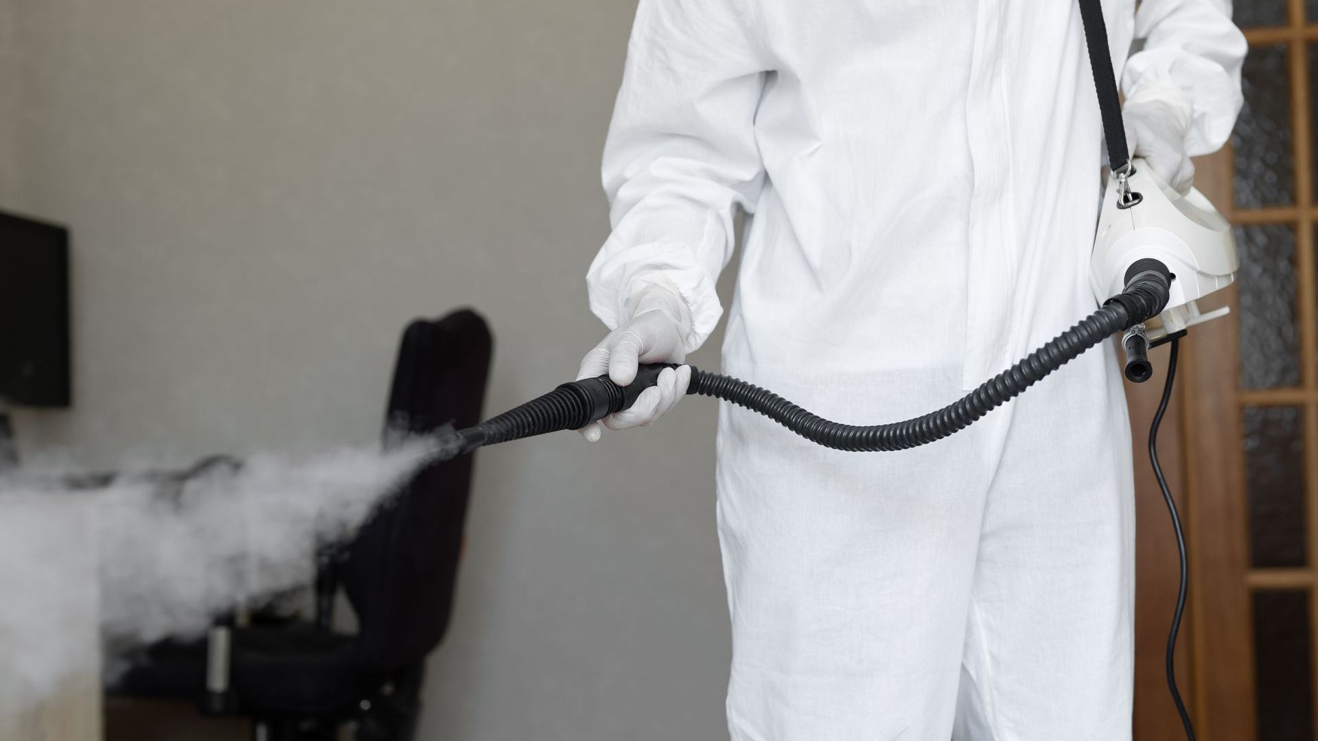A man in a protective suit is spraying a room with a sprayer.