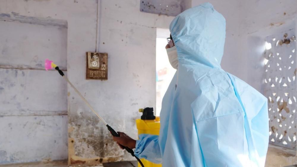 A man in a protective suit and mask is cleaning a wall.