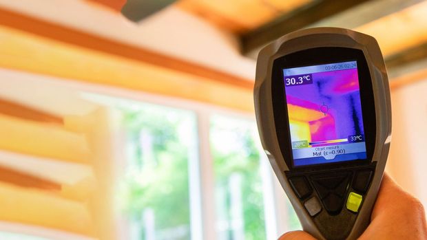 Hand holding a thermal imaging camera, showing a colorful heat map of a window, detecting potential leaks.