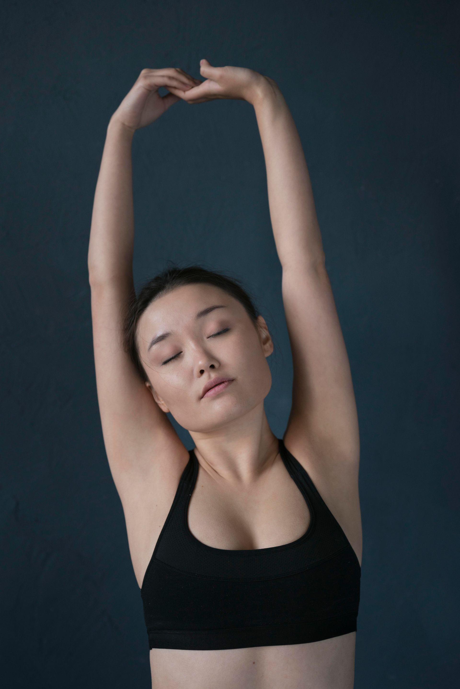 A woman in a black sports bra is stretching her arms.