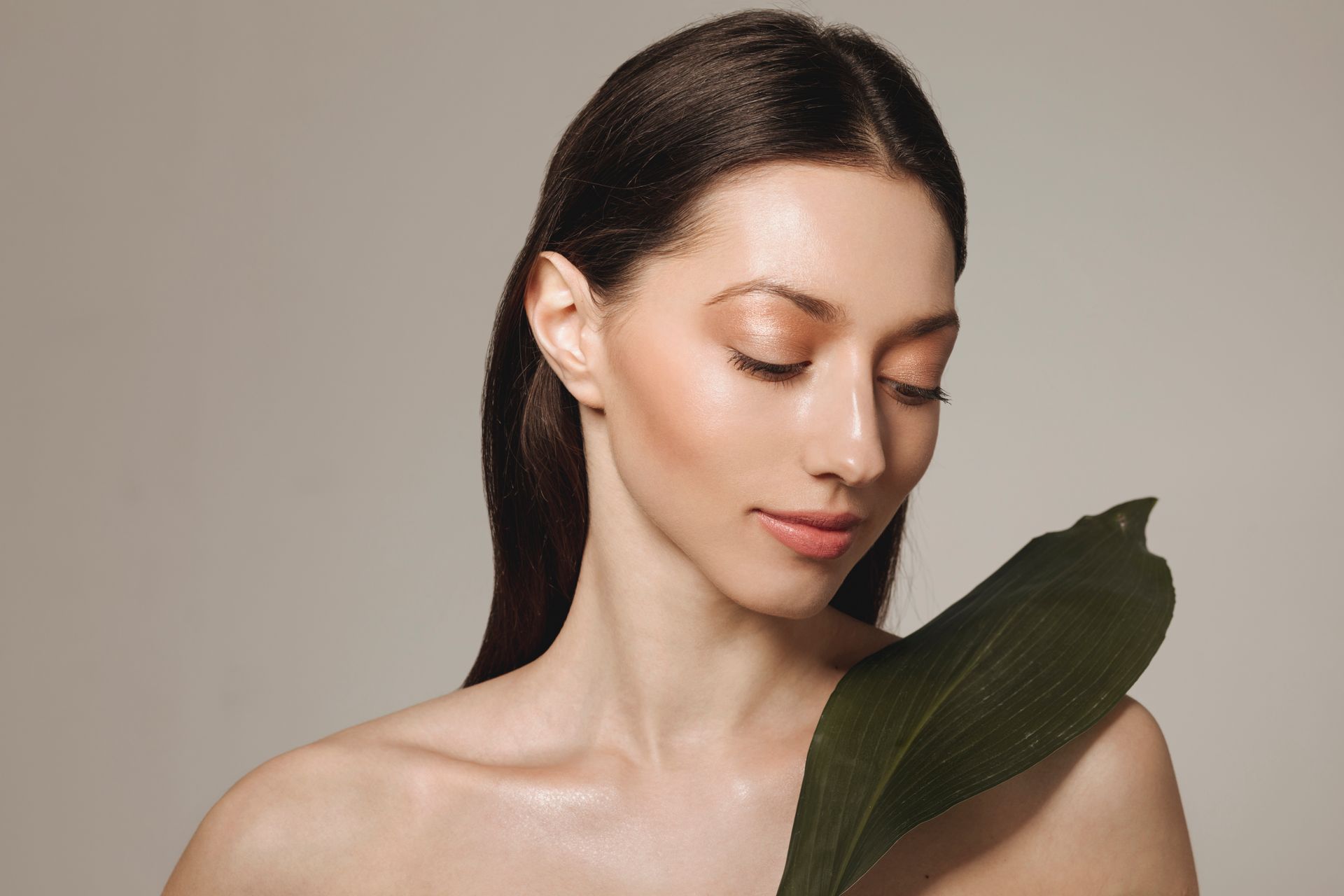 A woman is holding a green leaf in front of her face.