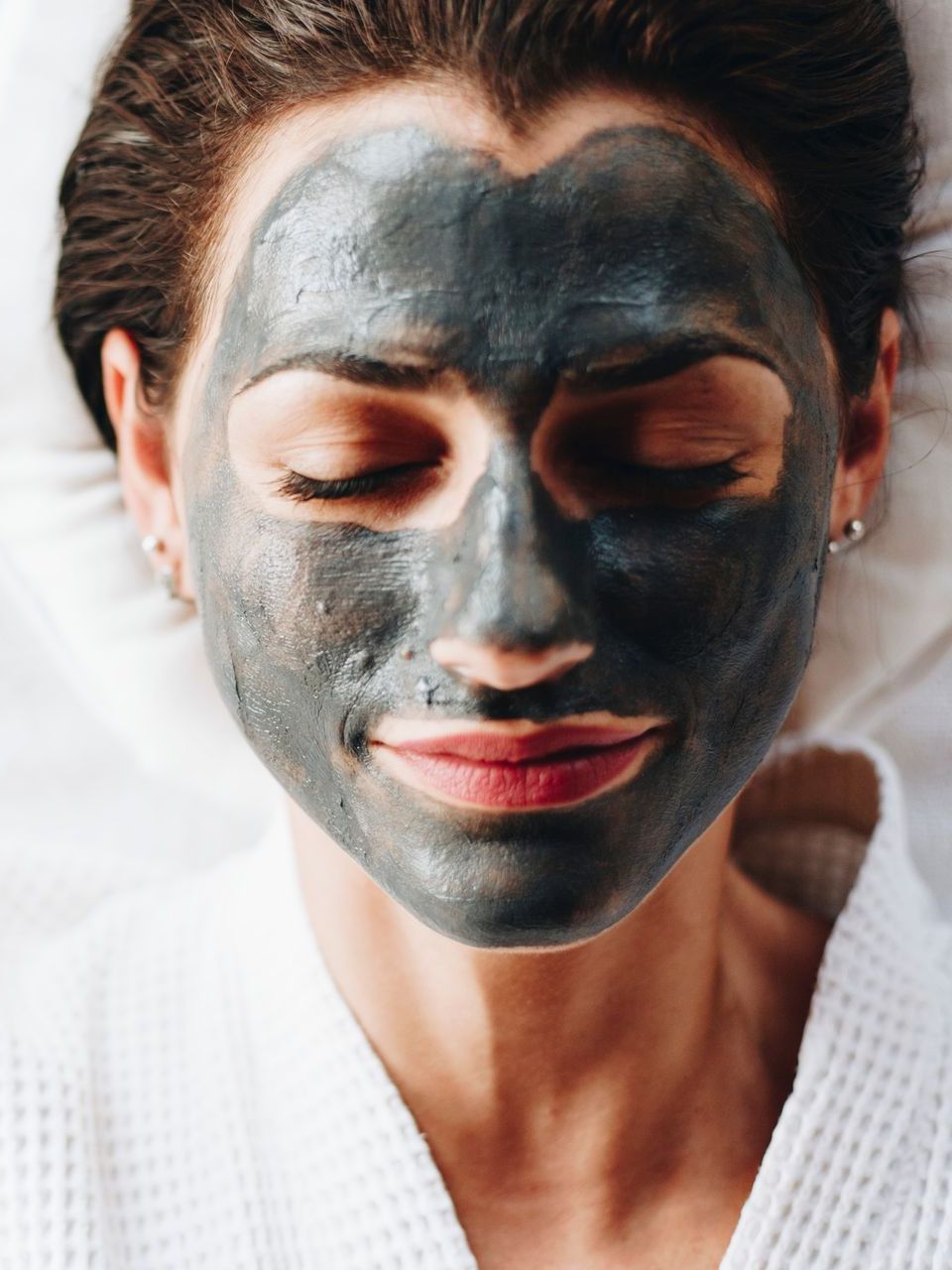 A woman is laying on a bed with a black mask on her face.