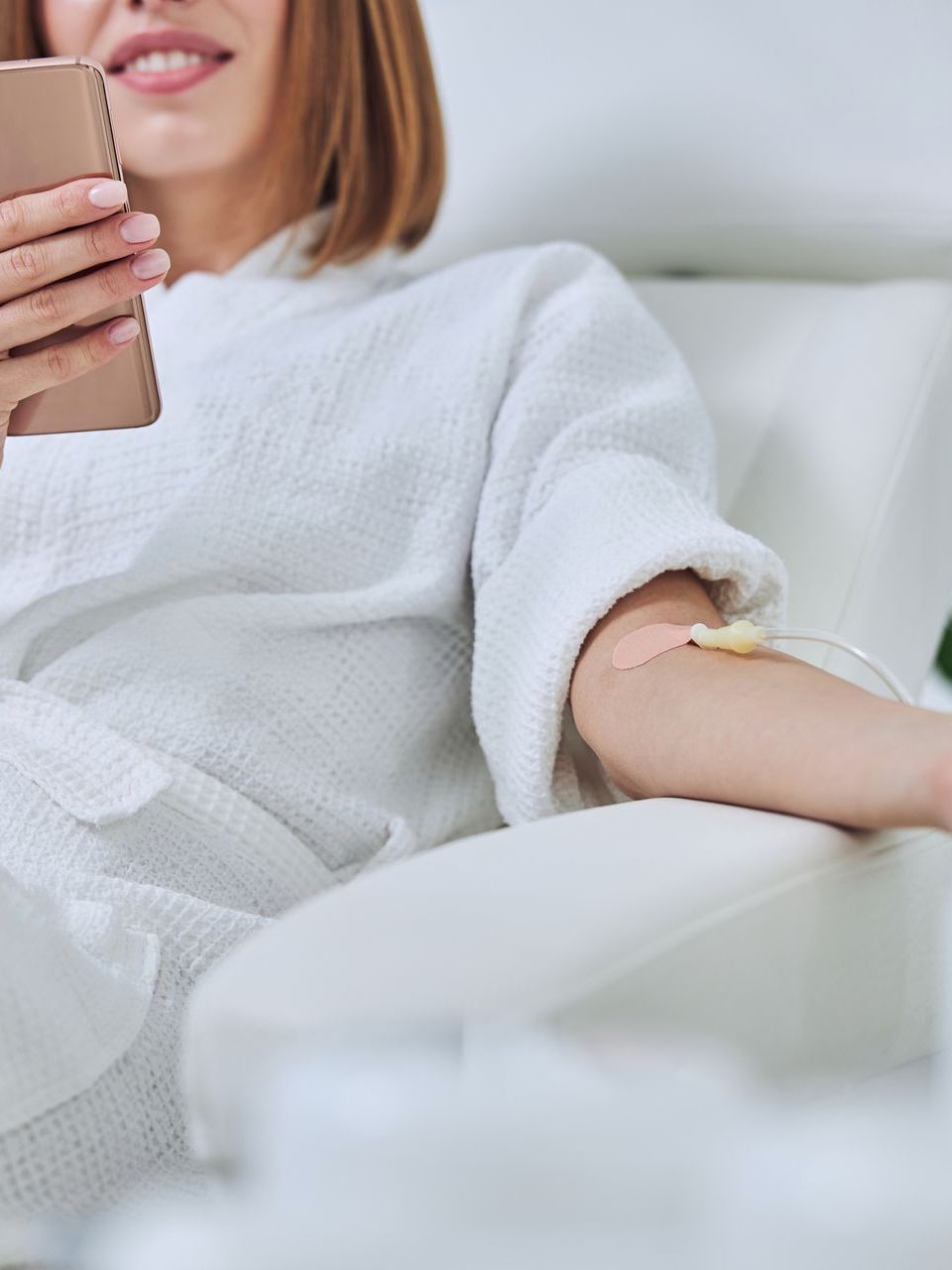 A woman is sitting on a couch with an iv in her arm and holding a cell phone.