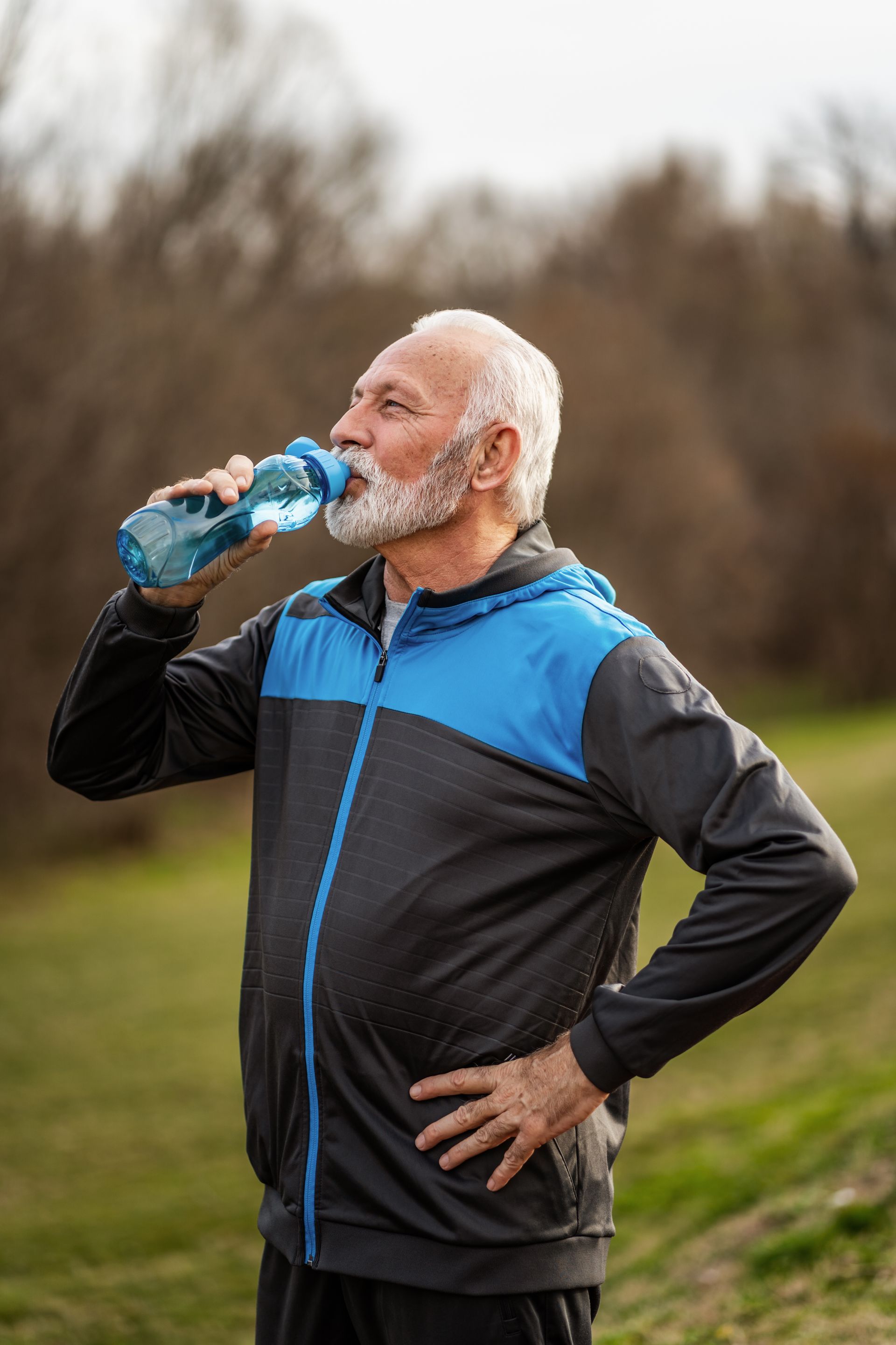 An elderly man is drinking water from a bottle in a park.