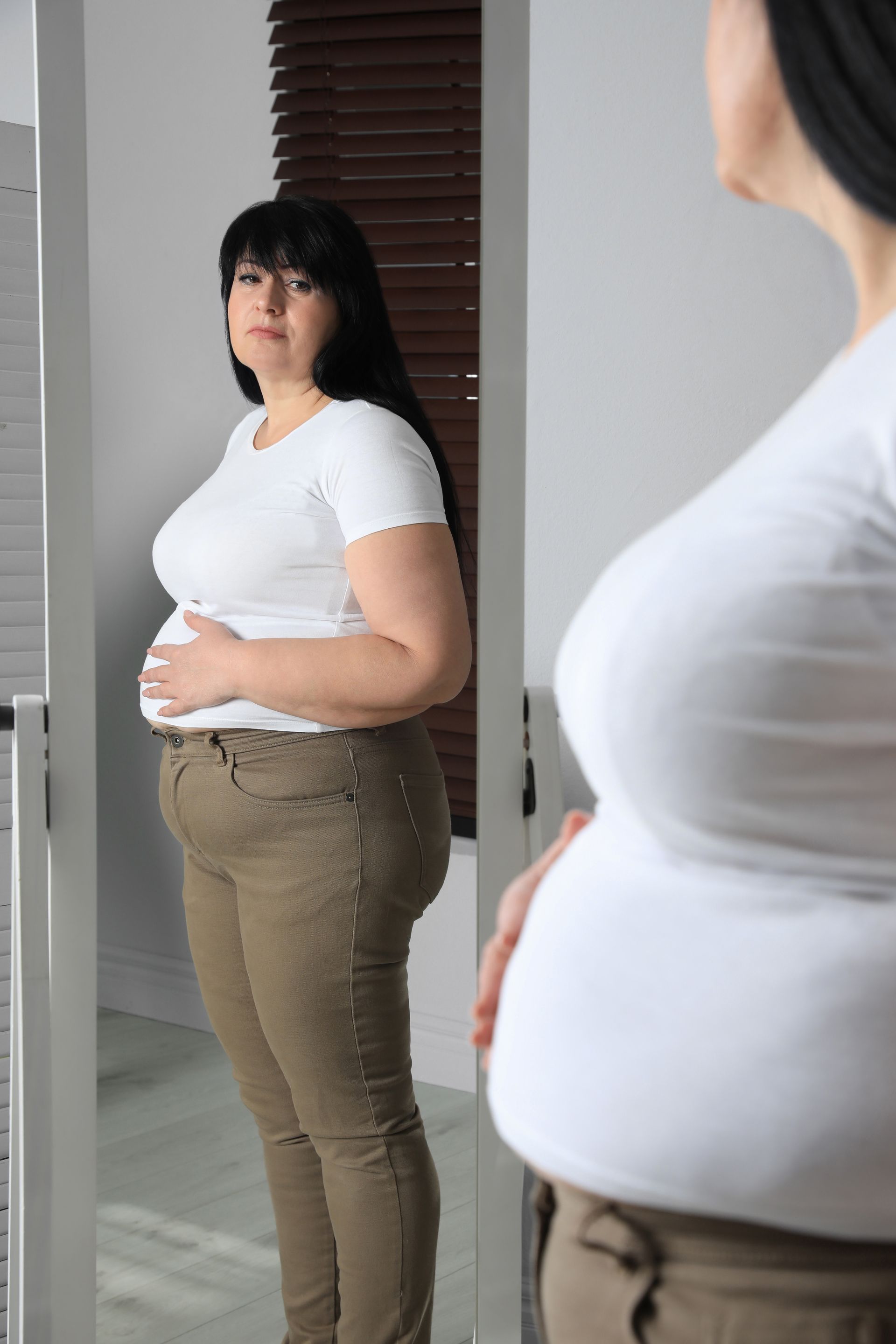 A pregnant woman is standing in front of a mirror holding her belly.