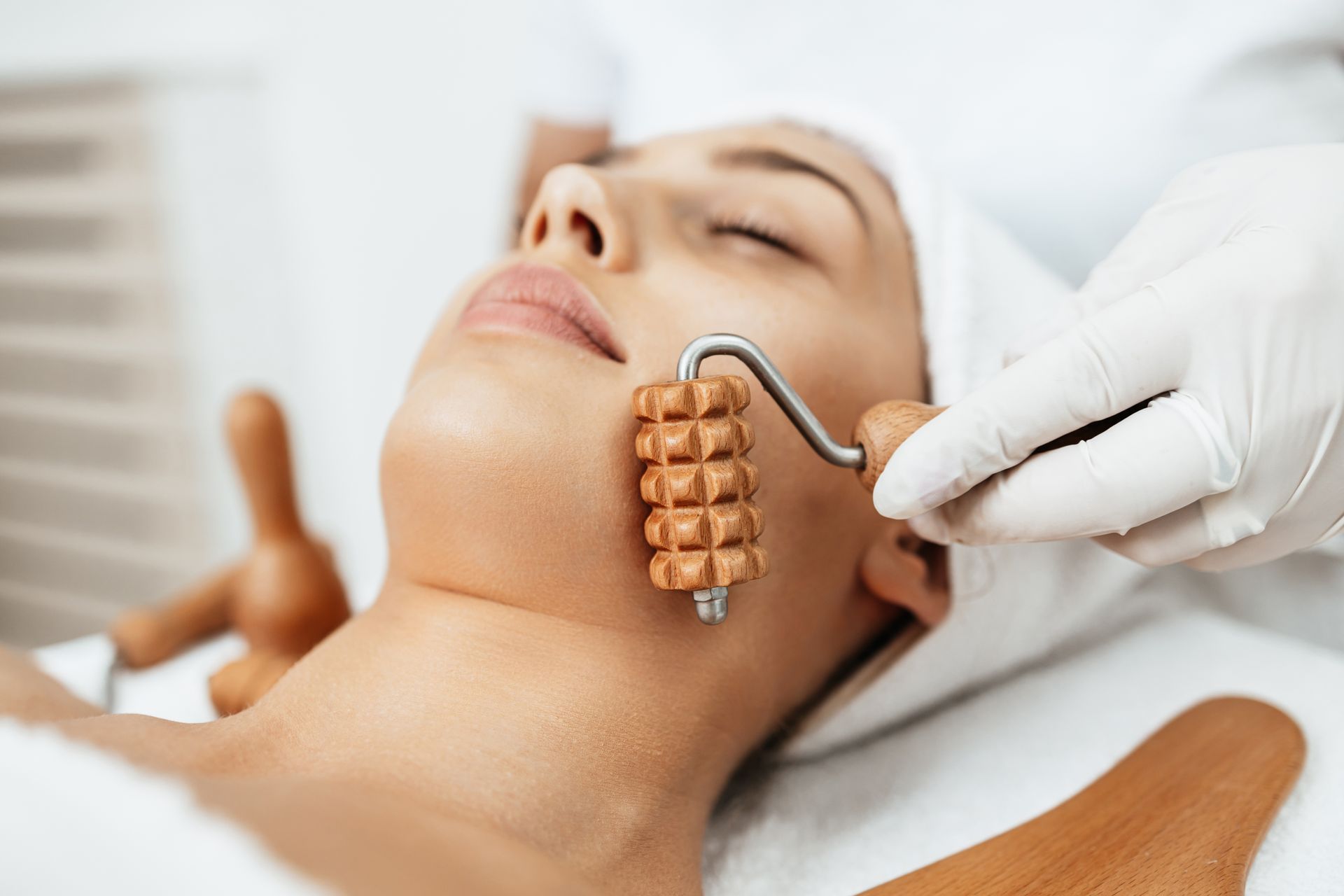 A woman is getting a massage with a wooden roller on her face.
