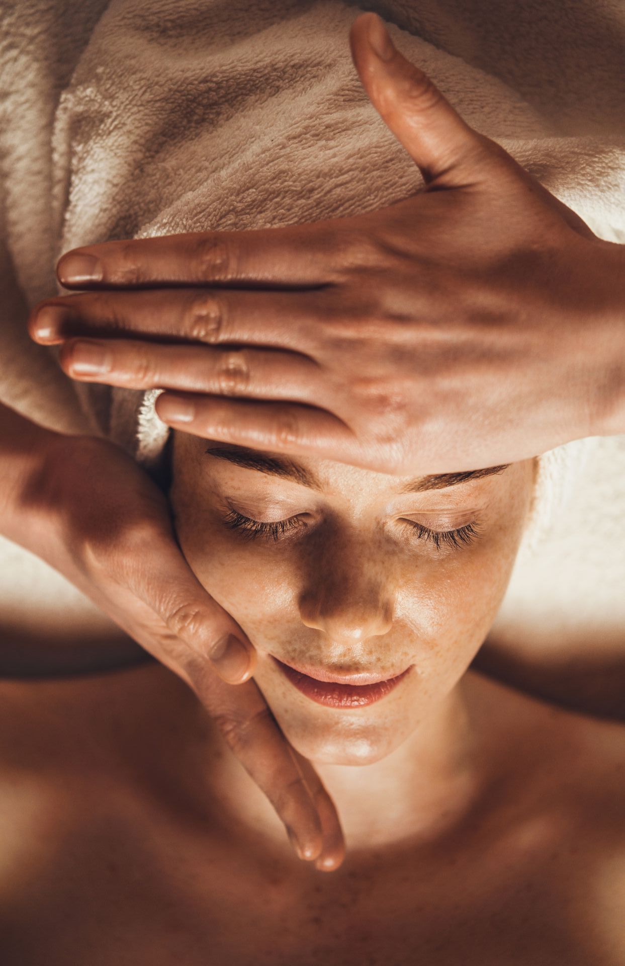 A woman is getting a facial massage at a spa with a towel wrapped around her head.