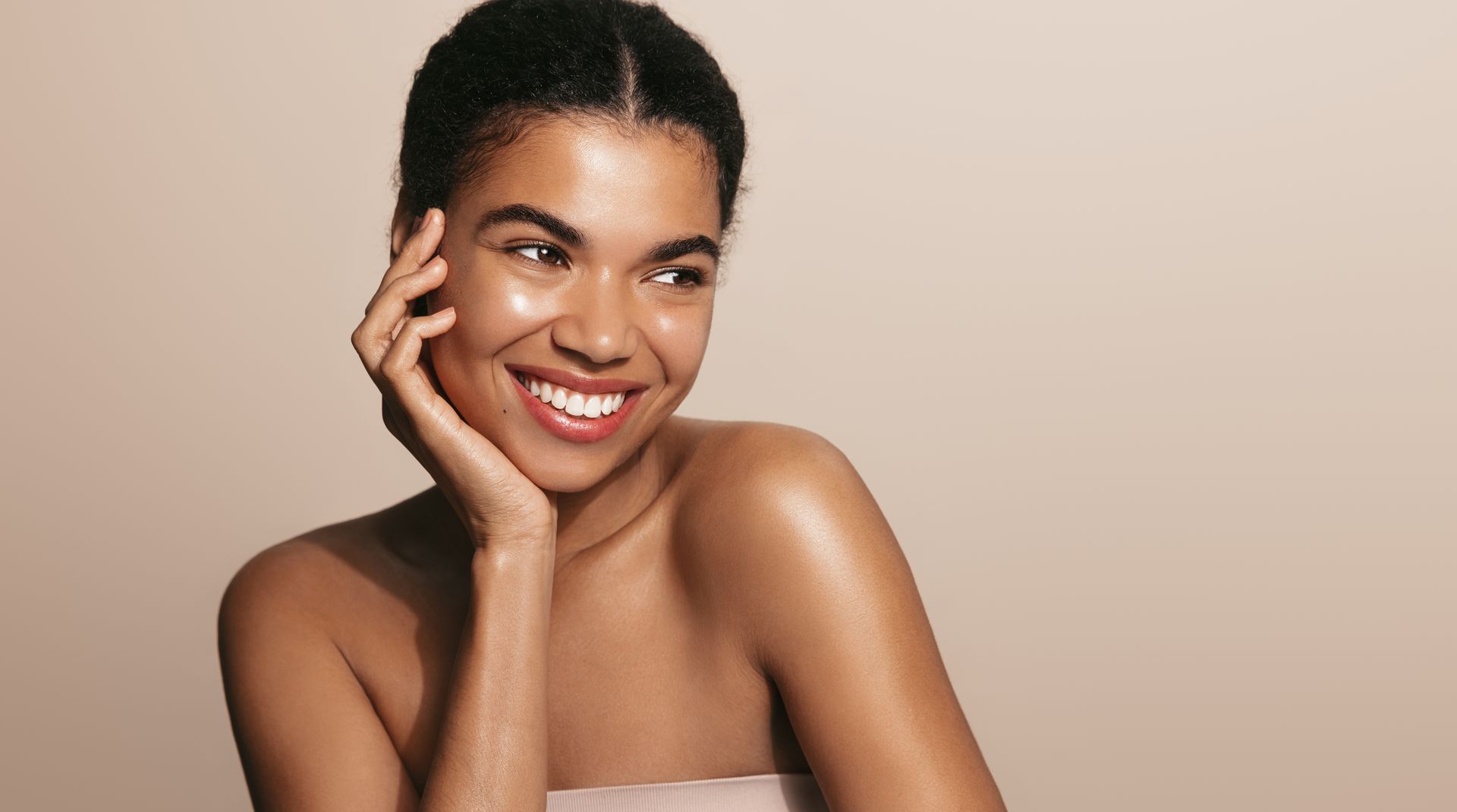 A woman is smiling and touching her face with her hand.