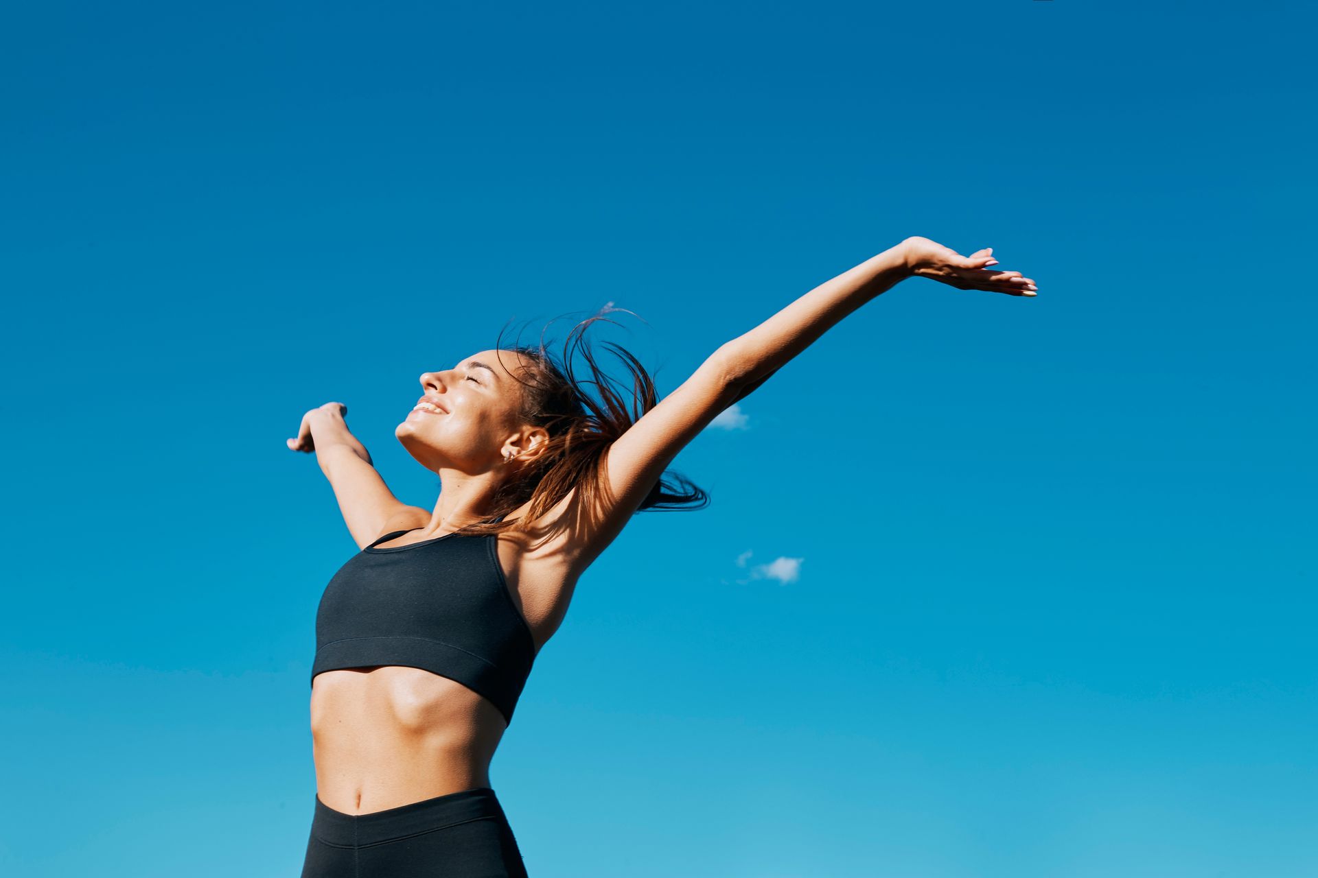 A woman is standing with her arms outstretched in front of a blue sky.