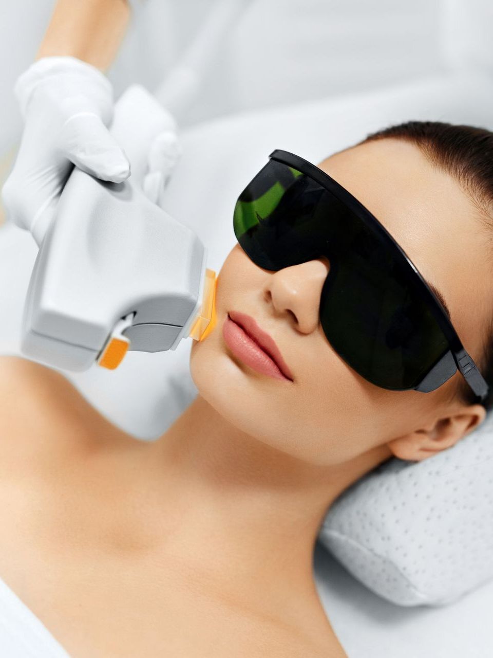 A woman wearing sunglasses is getting a laser treatment on her face