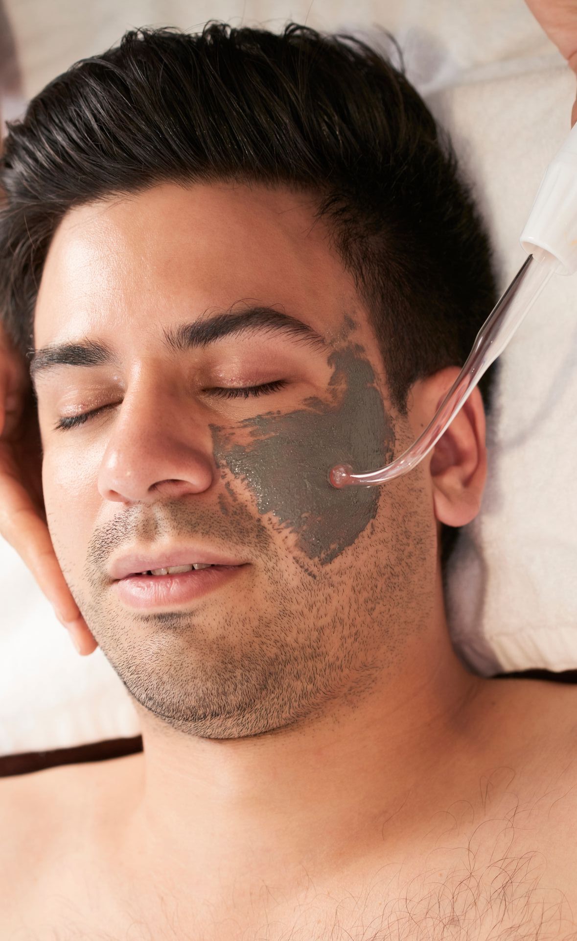 A man is getting a black mask on his face at a spa.