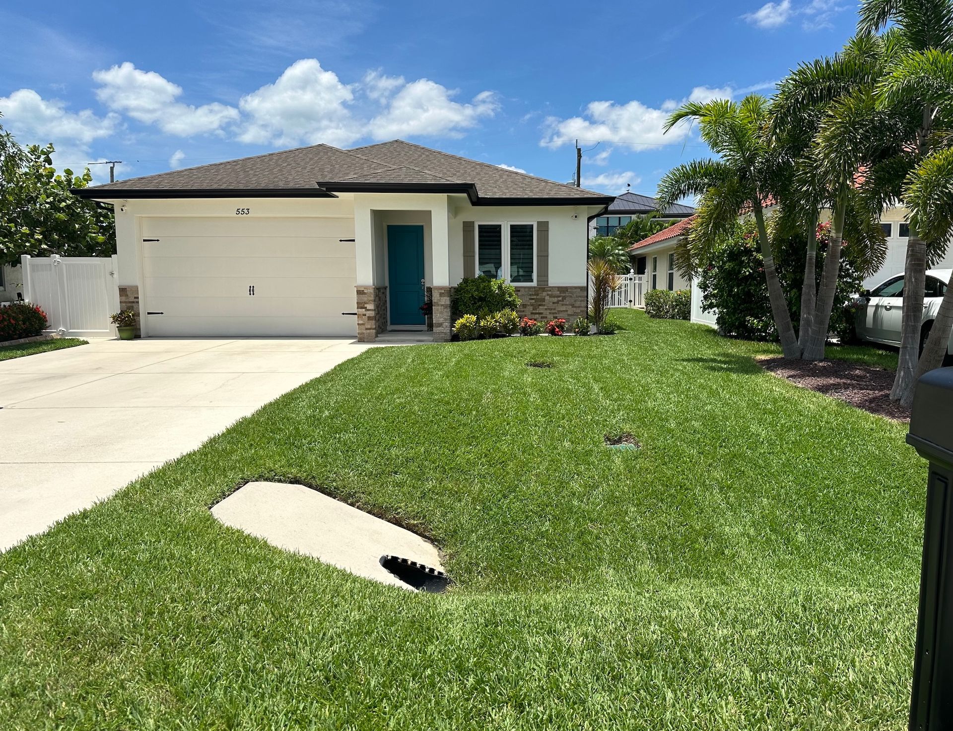 House with white garage door, teal door, and green lawn on a sunny day.