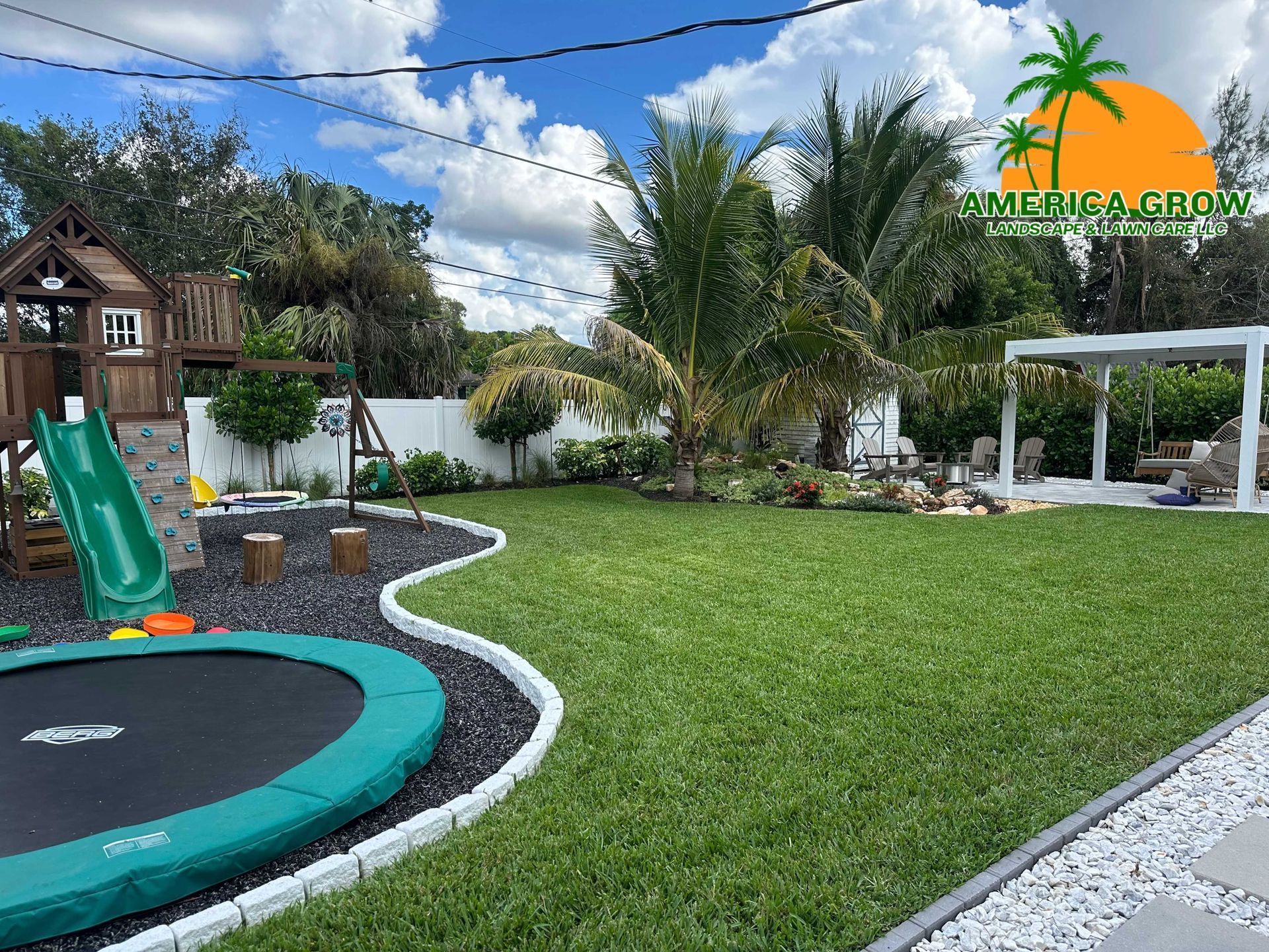 Backyard with playground, trampoline, and gazebo on a sunny day. Green grass and blue sky.
