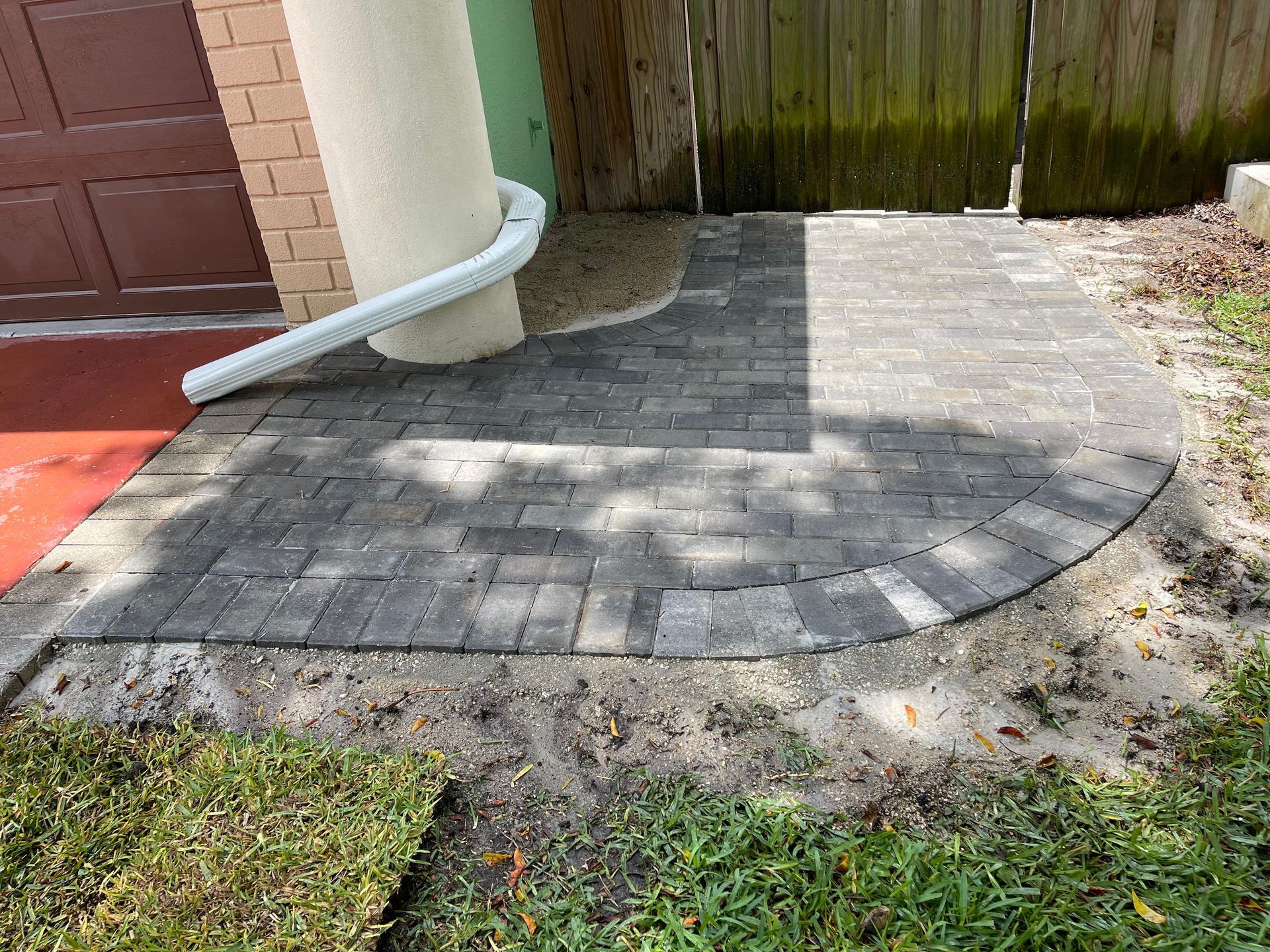Curved brick patio beside a garage with a white downspout and a fenced backyard.