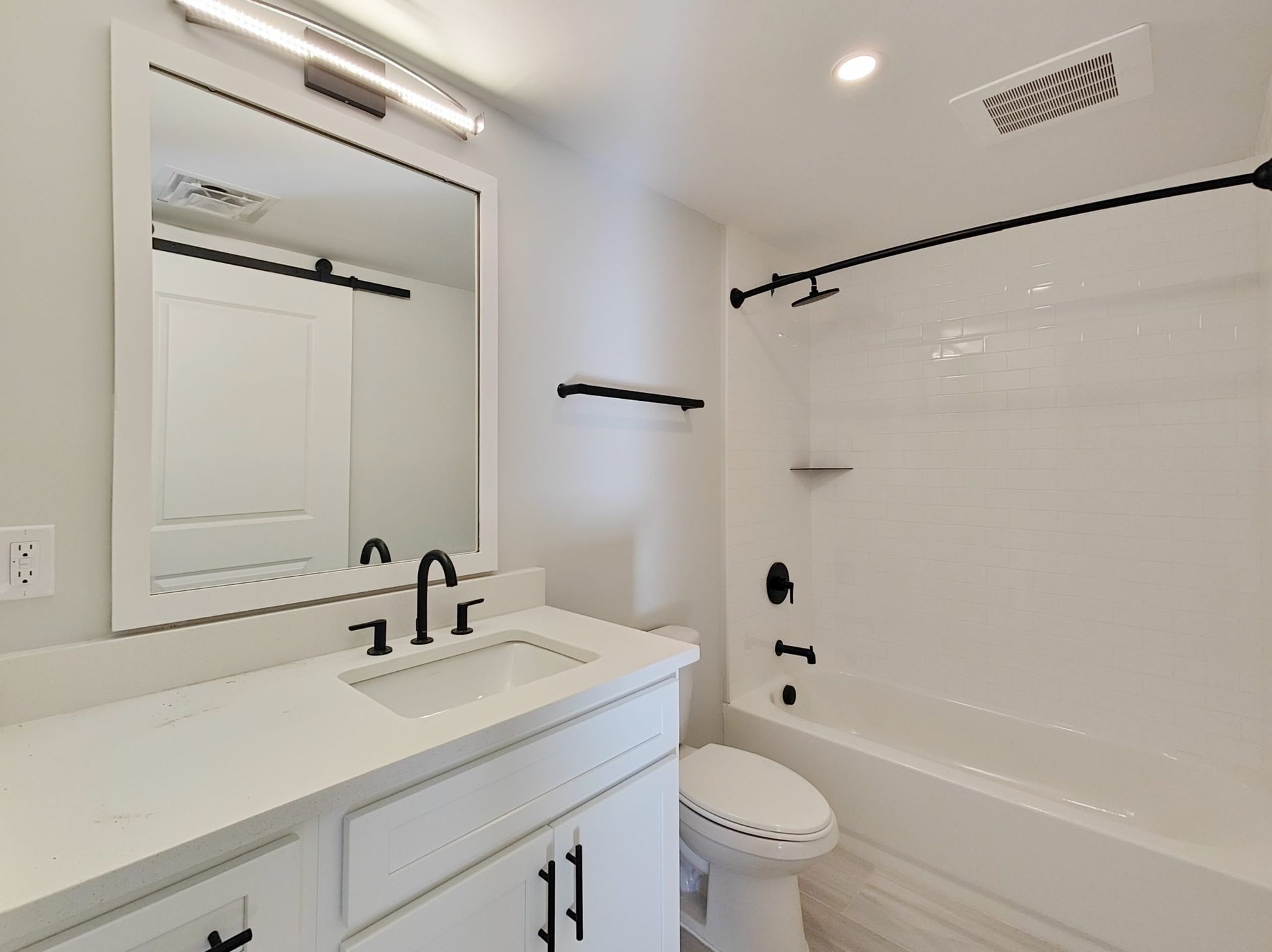 White bathroom with vanity, mirror, tub, toilet, and black fixtures.