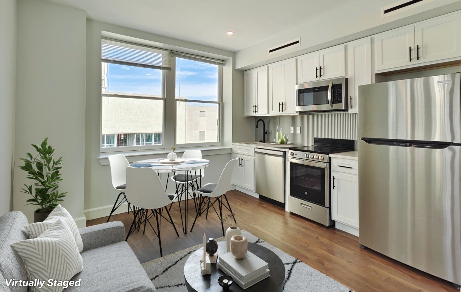 Modern apartment kitchen and dining area with stainless steel appliances and white cabinets.