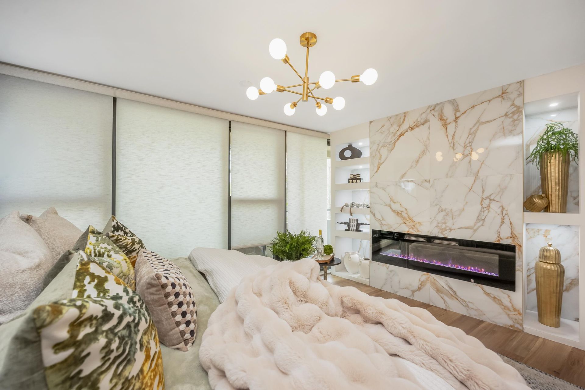 Bright modern bedroom with tufted bed, marble fireplace wall, and gold chandelier
