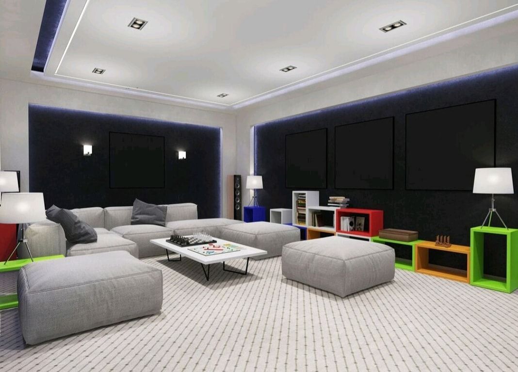 Modern living room with dark walls, gray sectional, white rug, and colorful cube shelves under recessed lights