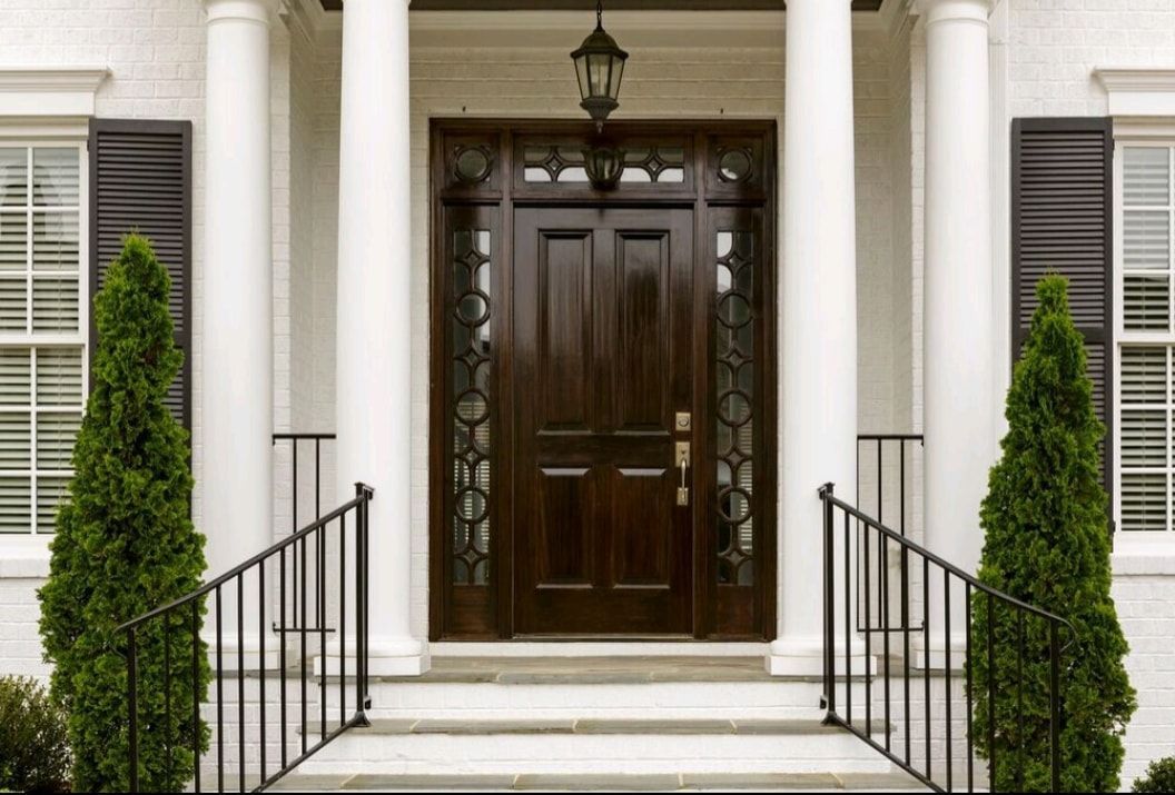 Front entrance with dark wooden door, white columns, and trimmed shrubs flanking the steps.