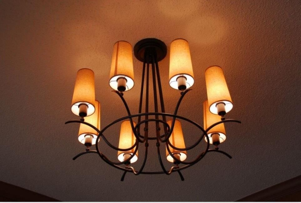 Black chandelier with six orange-glass shades hanging from a ceiling.