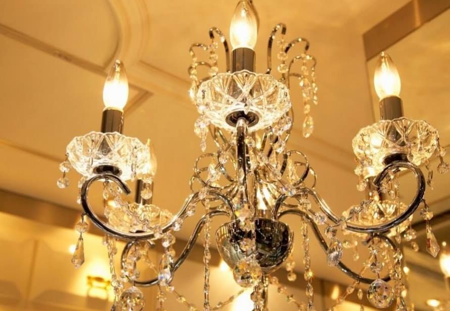 Crystal chandelier with lit bulbs hanging from a ceiling, reflecting warm light.
