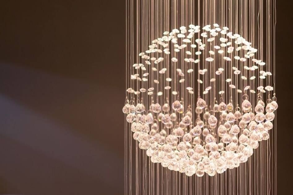 Glowing spherical crystal chandelier with hanging beads against a dark brown background