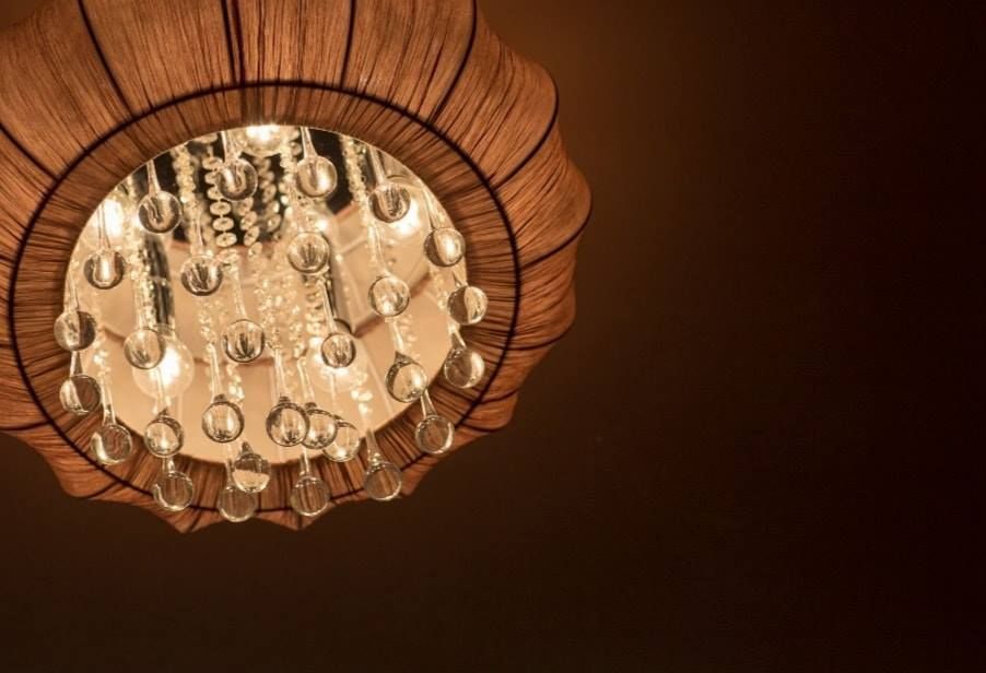 Round chandelier with dangling crystal pendants and a warm brown lampshade glowing against a dark ceiling.